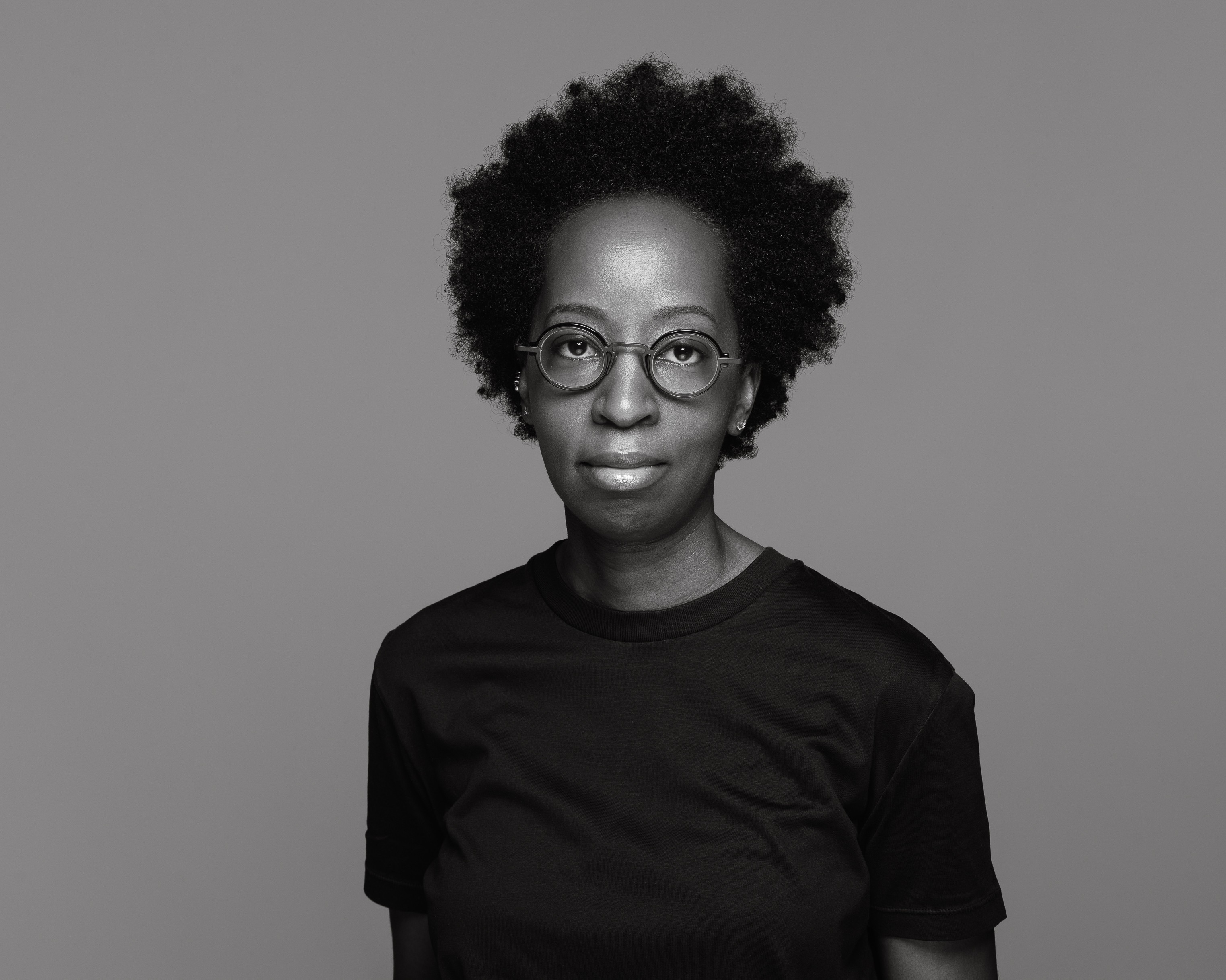 Black and white photo of a Black woman with curly hair and round glasses.