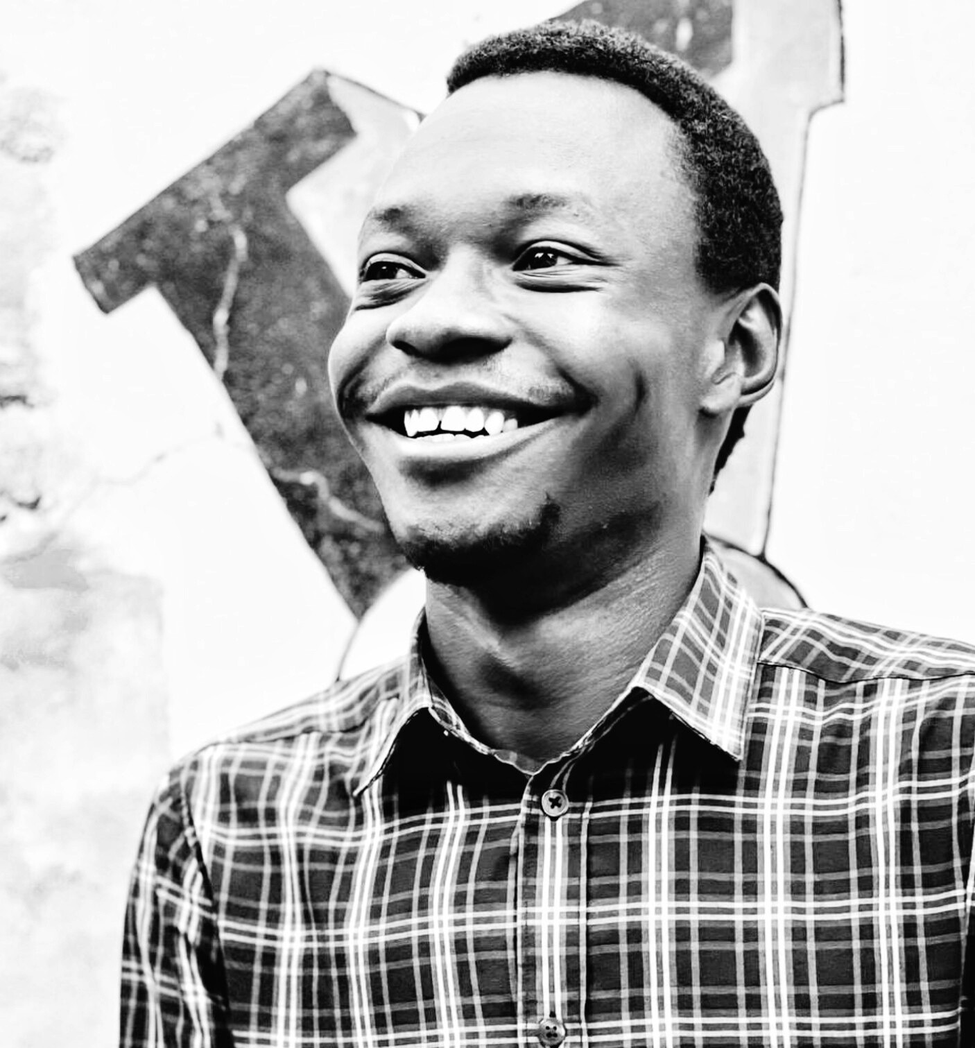 A smiling Black man in a plaid shirt, in a black and white photo.