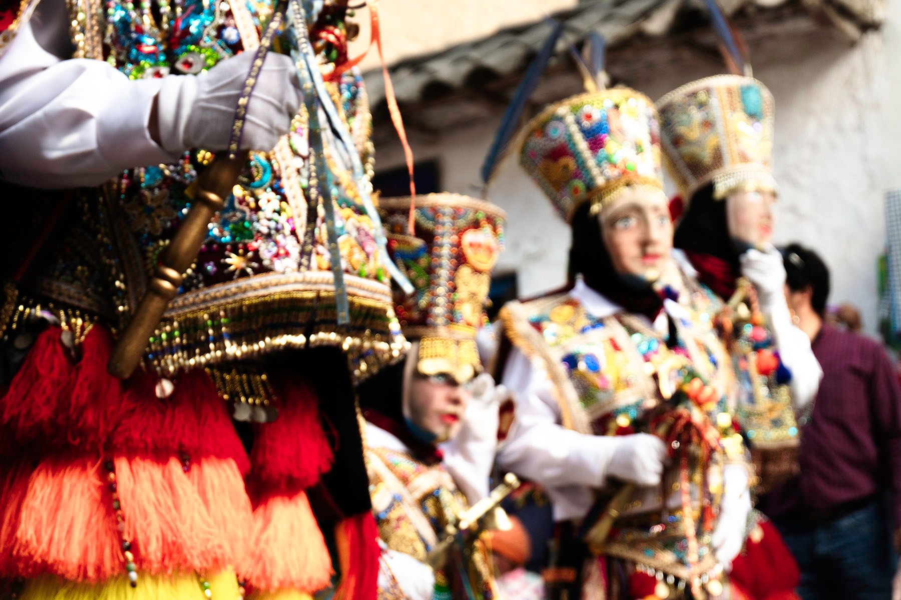 People in vibrant, ornate traditional costumes with tall hats and masks.