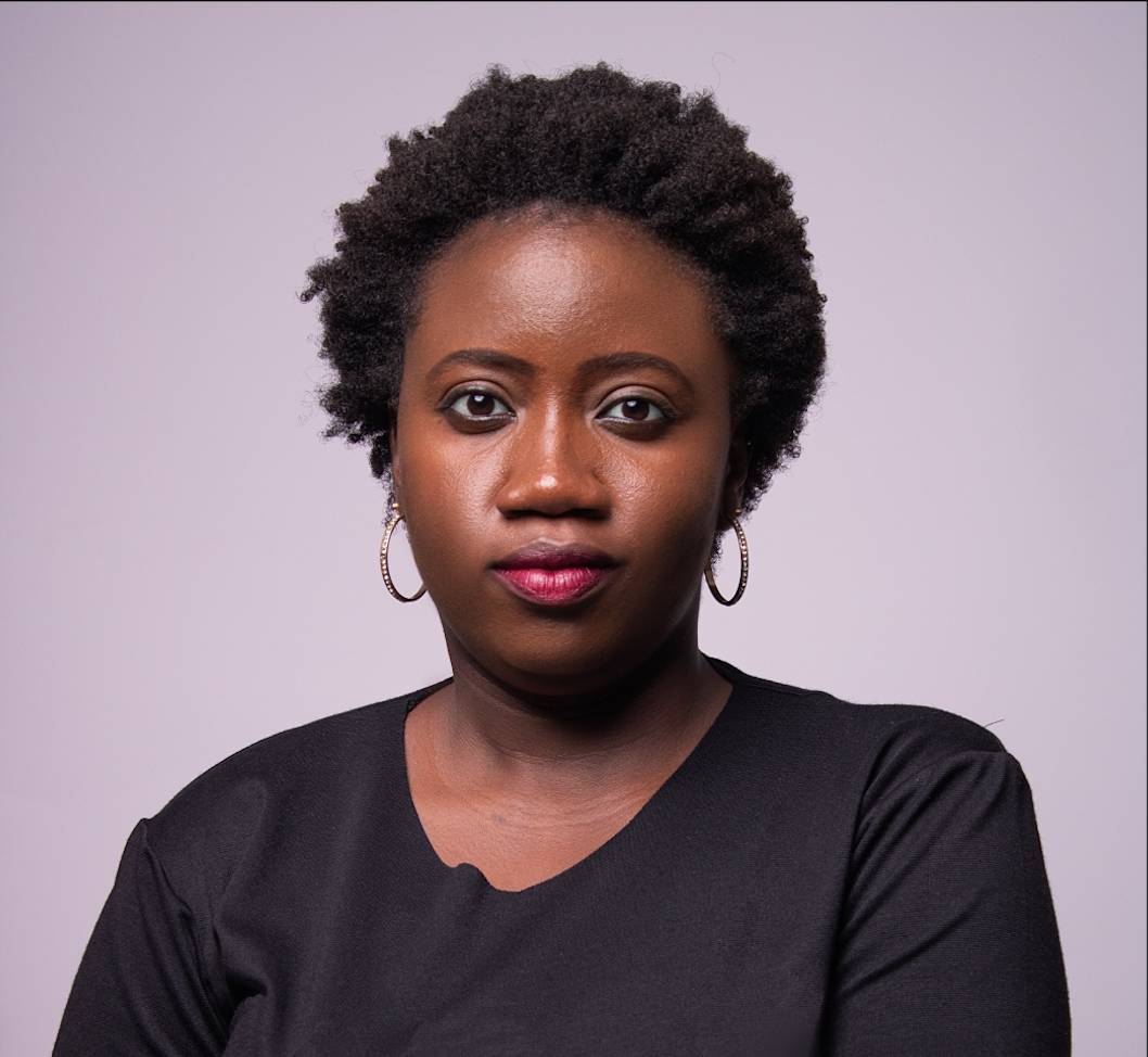 Headshot of a woman with dark skin, short curly hair, a black top, and hoop earrings.