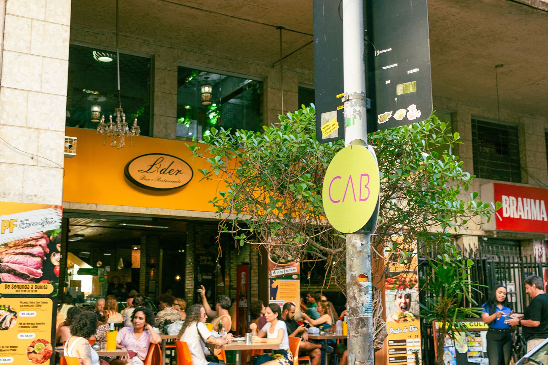 A lively scene outside Lider Bar & Restaurante, featuring a yellow facade and numerous people dining at outdoor tables on the sidewalk.