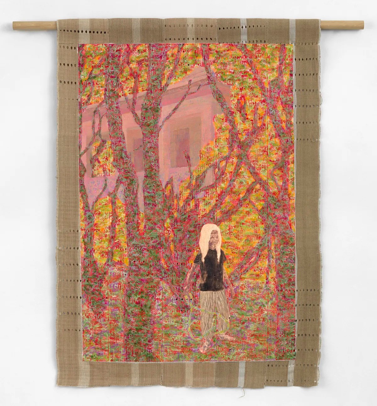 A vibrant textile wall hanging depicts a figure with light hair in a colorful, textured forest, with a pink house in the background.