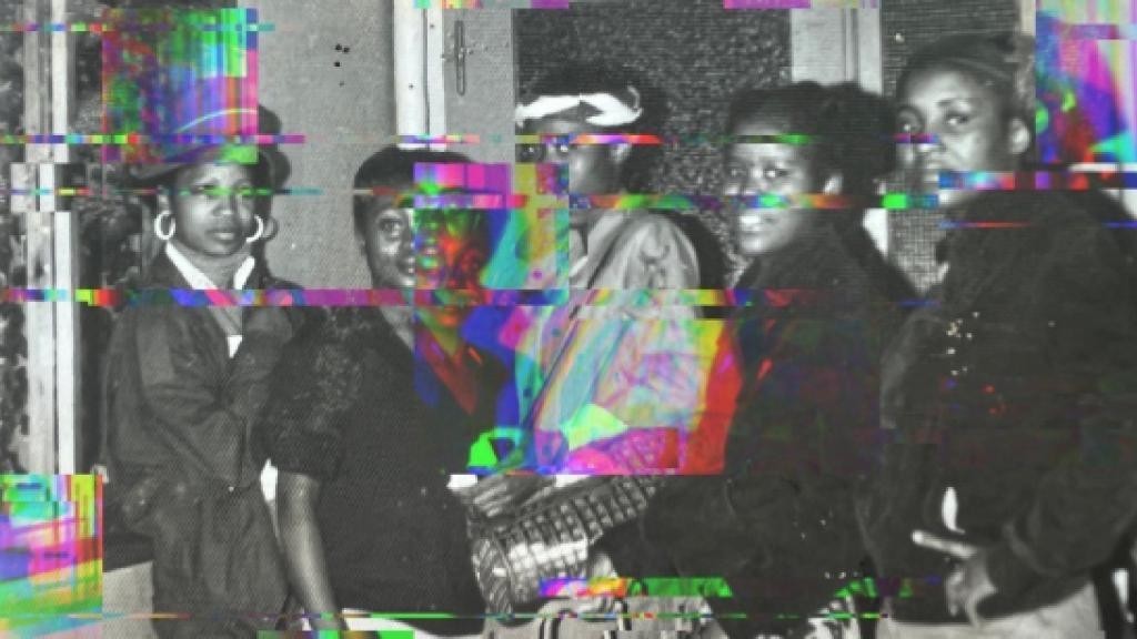 Black and white photo of several people, distorted by colorful digital glitches.