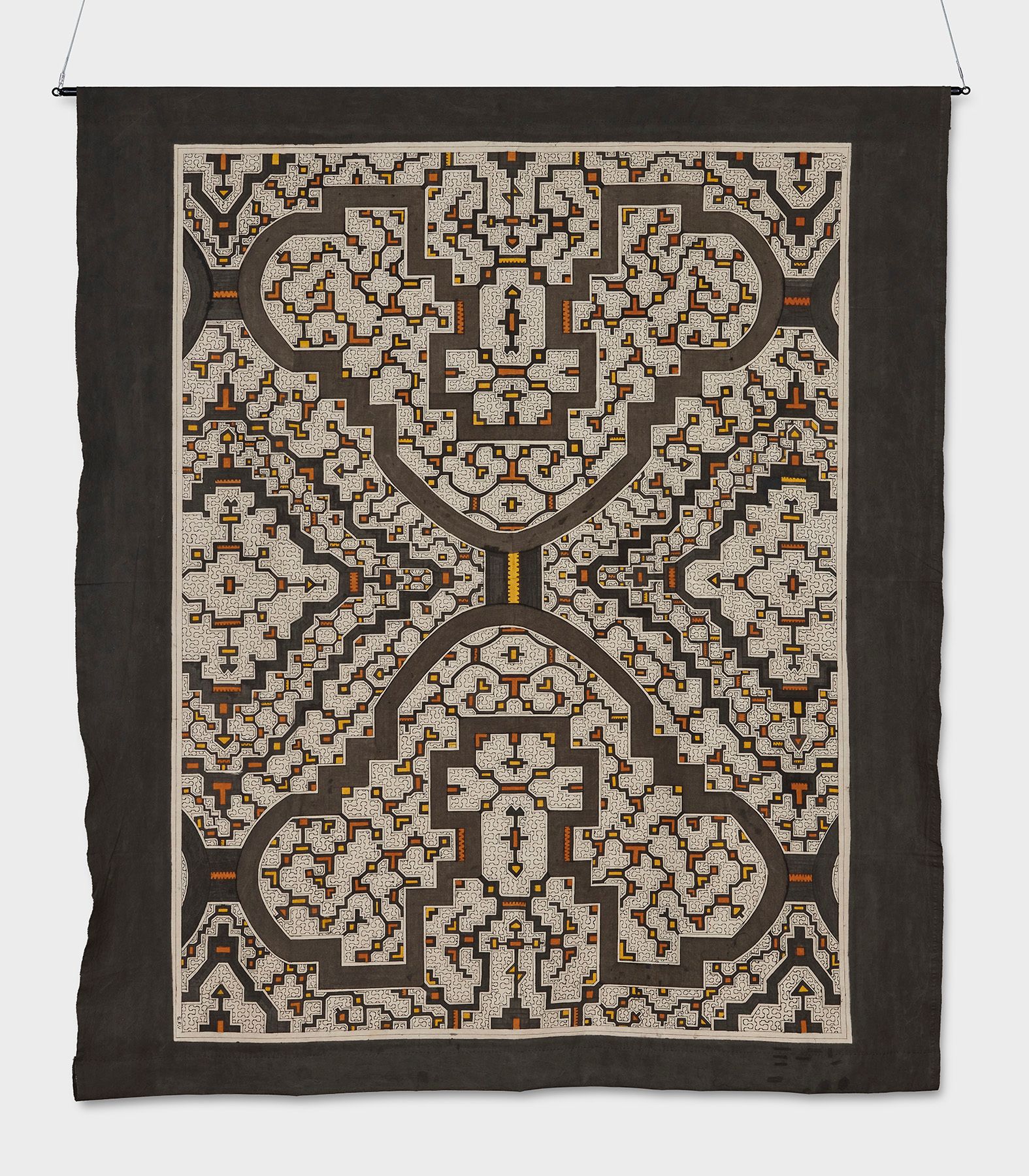 Hanging textile artwork featuring an intricate, symmetrical, maze-like pattern in brown, light grey, orange, and yellow.