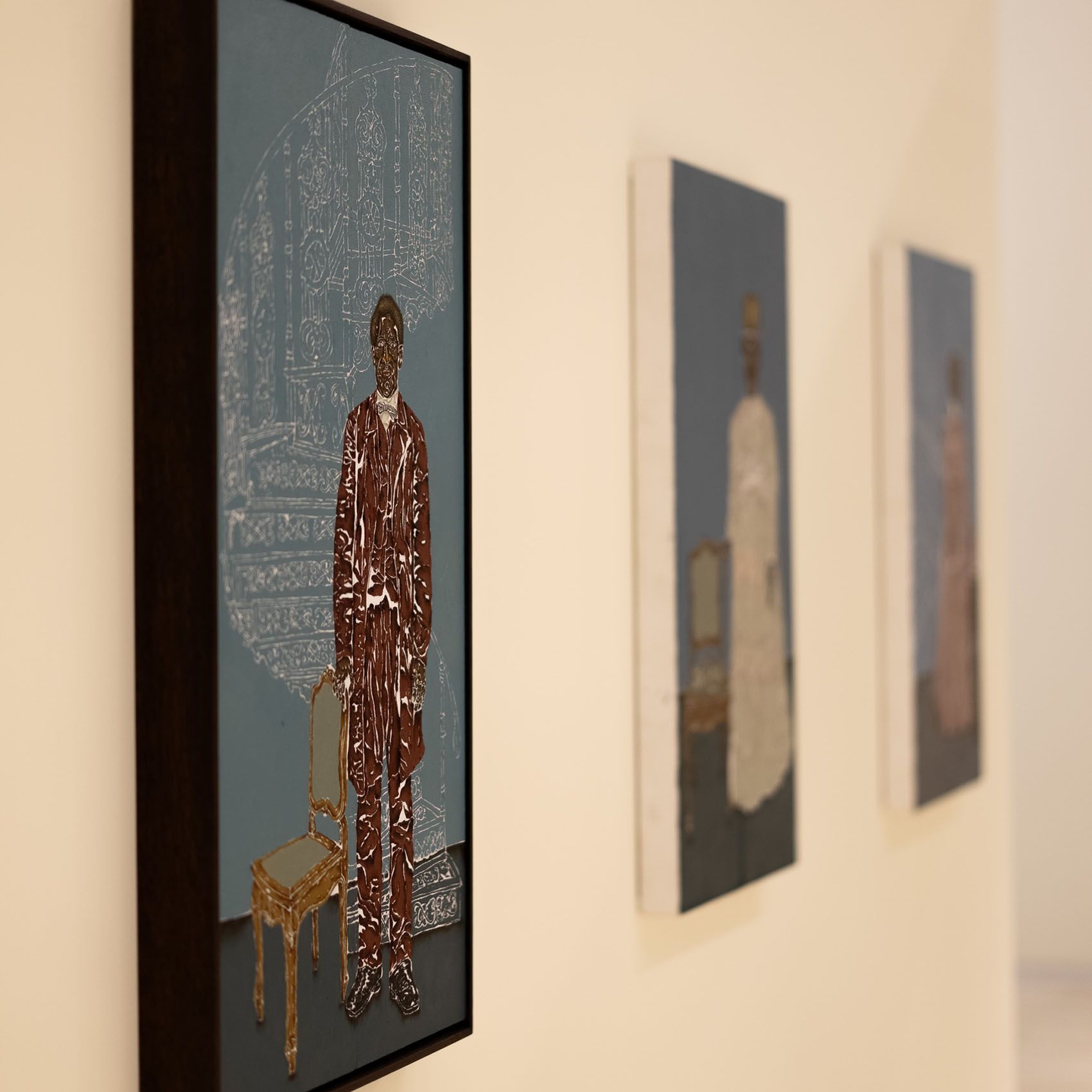 Three framed paintings on a light wall; the first depicts a stylized man in a textured brown suit next to a gold chair on a blue background.