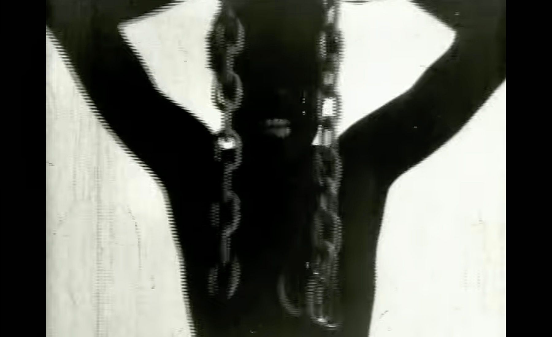Black silhouette of a person with raised arms, a thick chain draped over their shoulders.