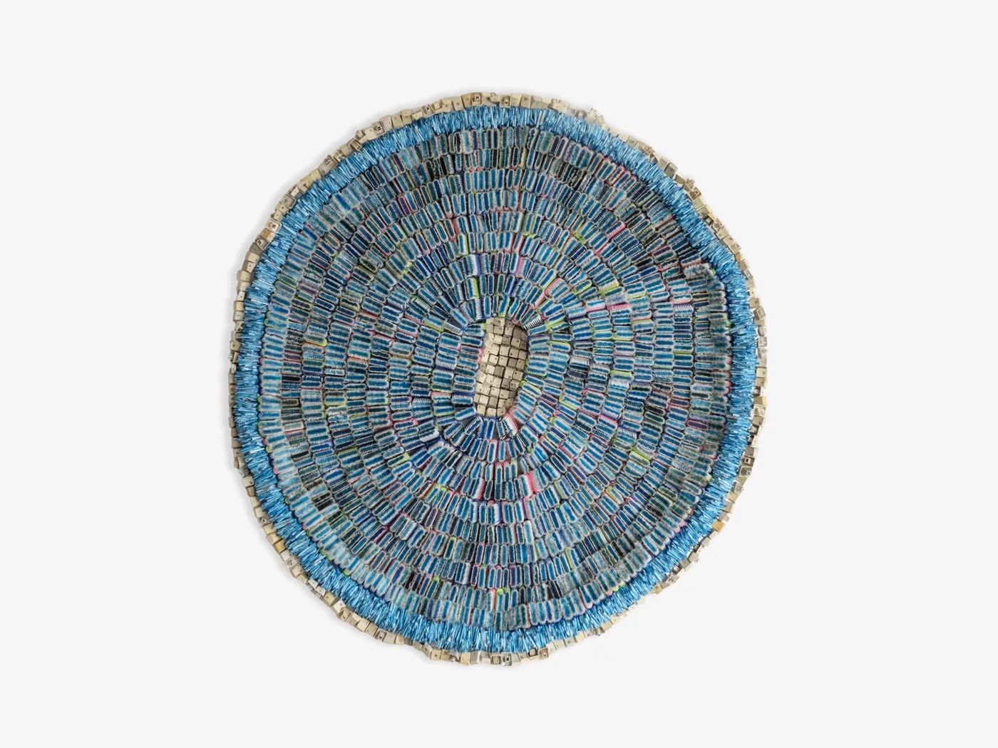 Circular artwork made of small blue and grey rectangular pieces arranged in concentric rings, with a central oval opening.
