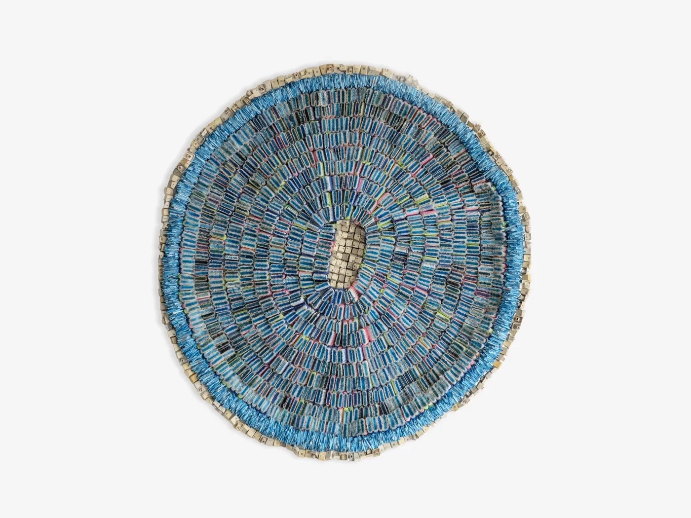 Circular artwork made of small blue and grey rectangular pieces arranged in concentric rings, with a central oval opening.