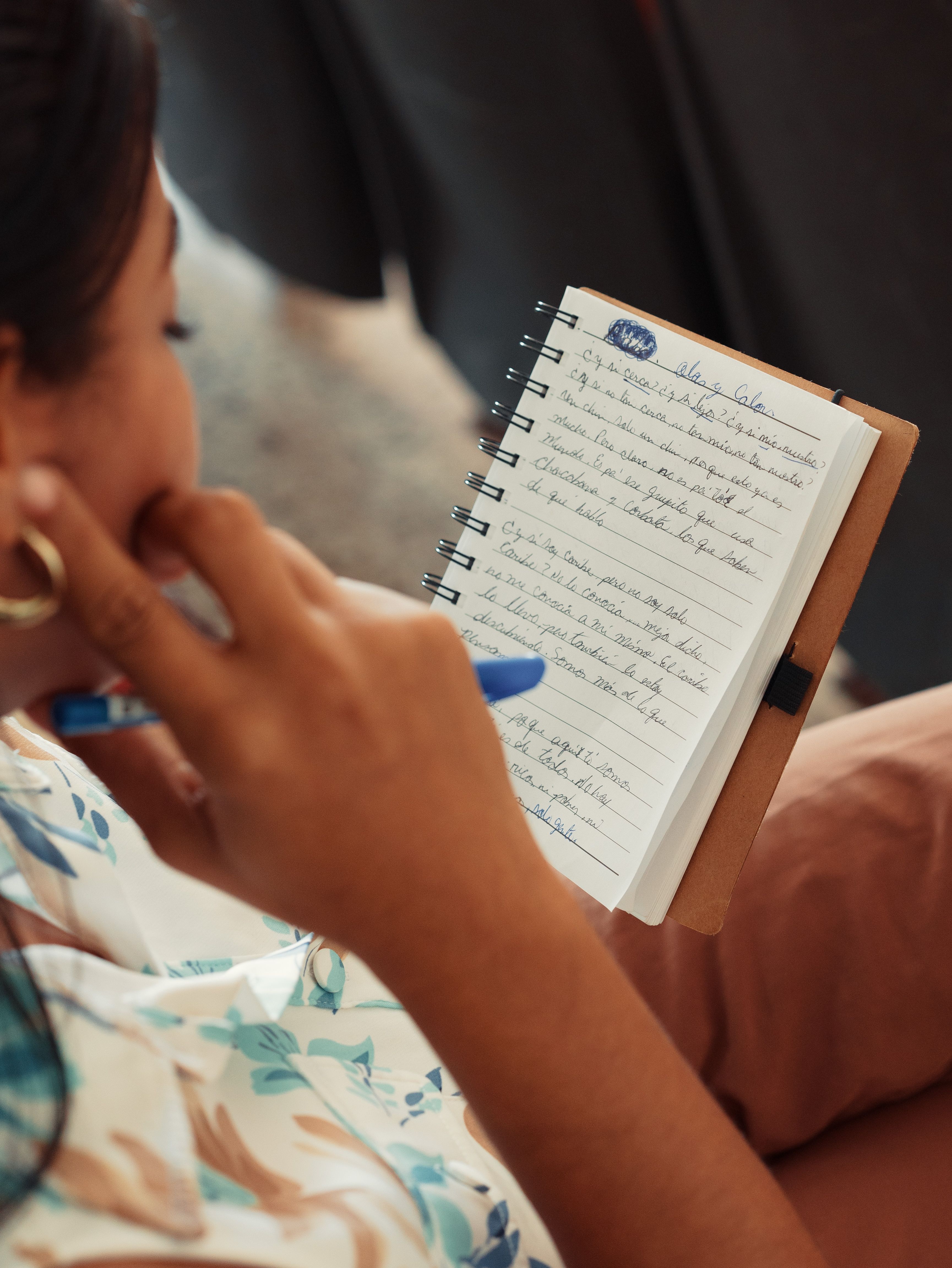 Close-up of a person writing in a small, spiral notebook with a blue pen.