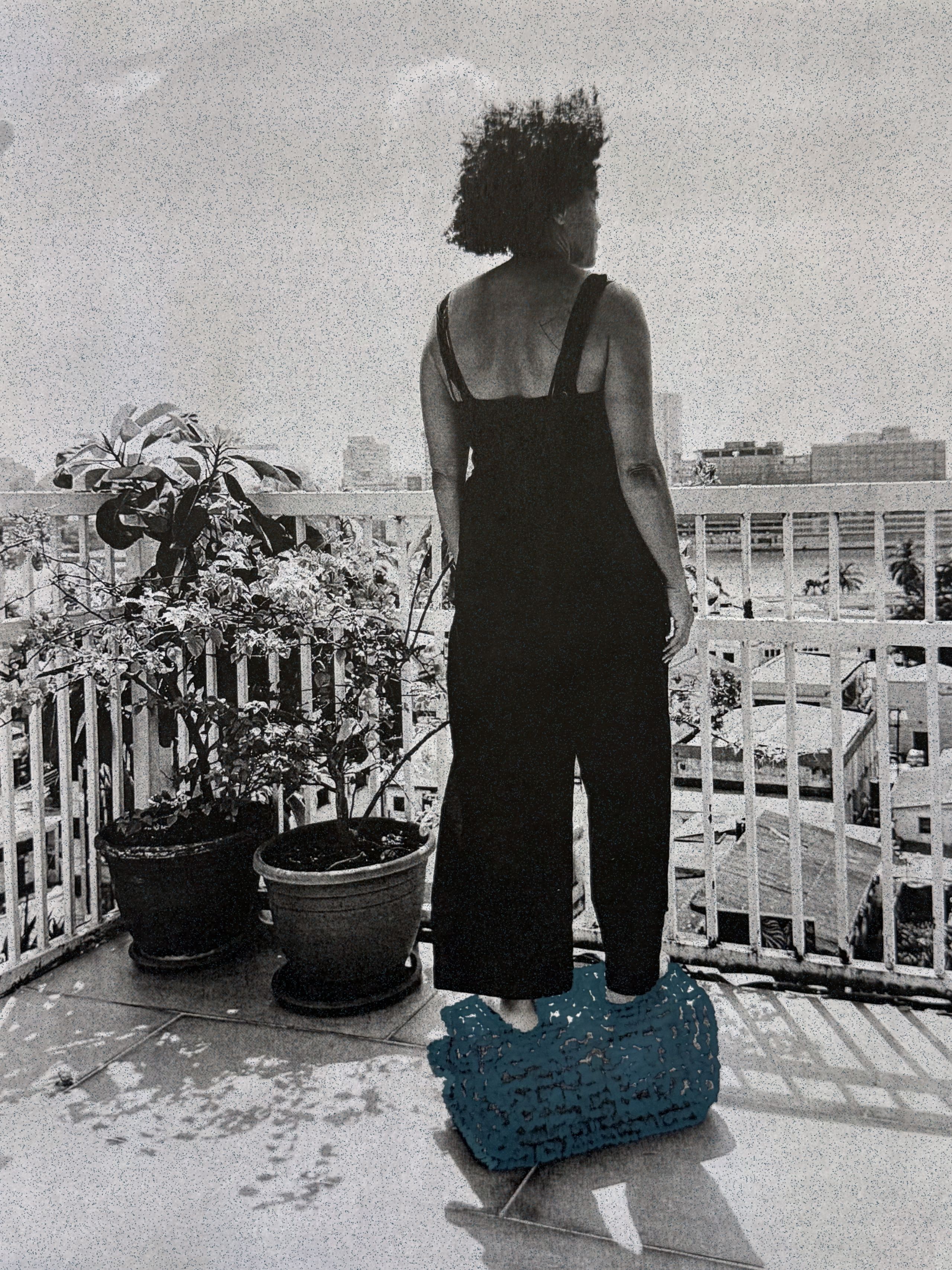Grainy monochrome image of a person in a black jumpsuit standing on a teal woven object on a balcony, looking at a city skyline.