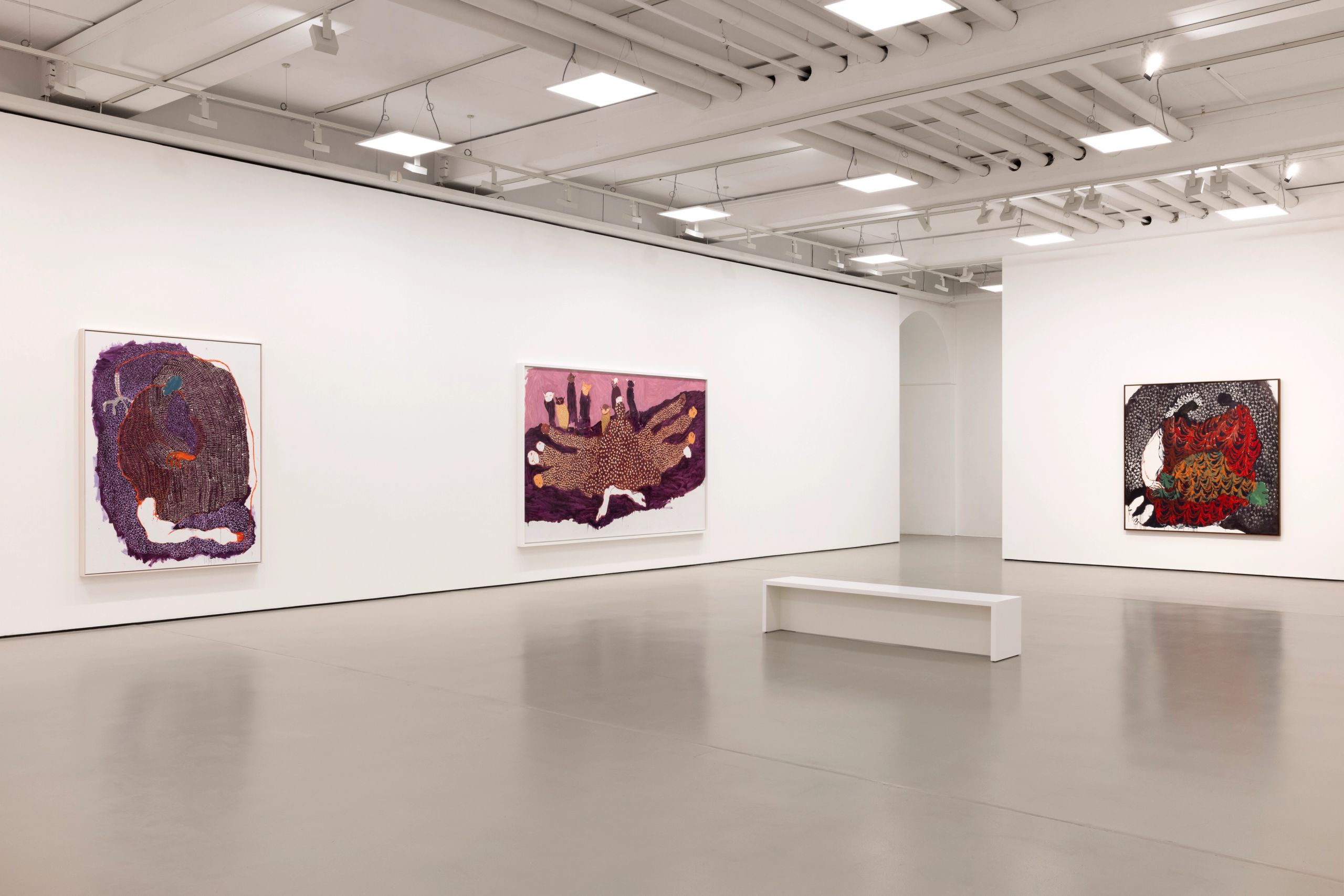 Three abstract paintings hang on white walls in a brightly lit art gallery with a white bench.