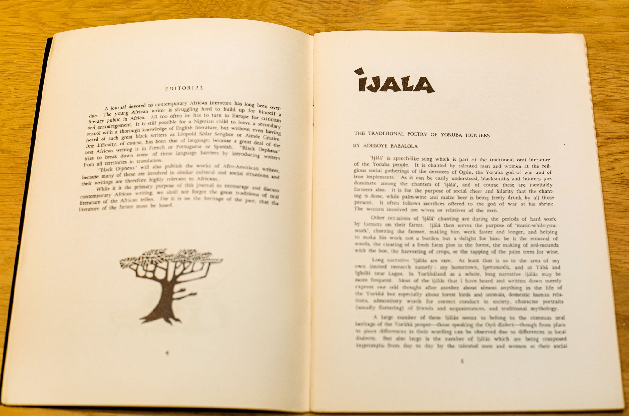 An open book with two pages of text. The left page is an editorial with a tree illustration, and the right page features an article titled "IJALA: The Traditional Poetry of Yoruba Hunters."