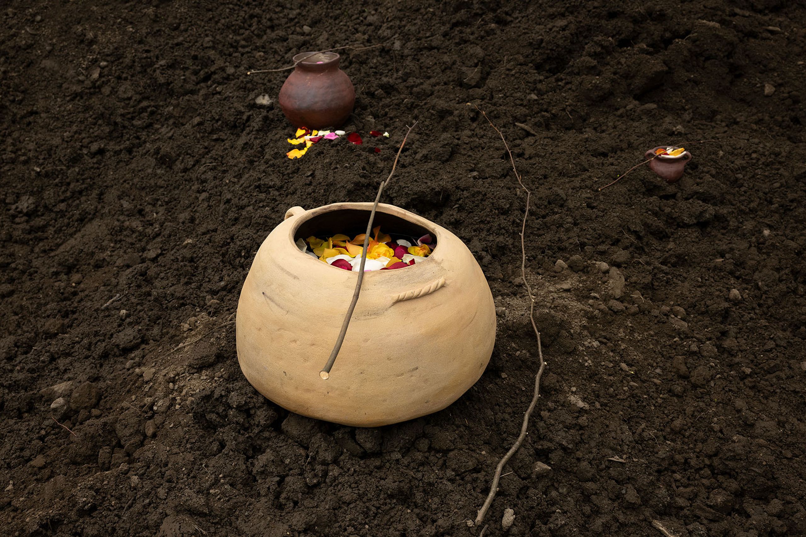 Three clay pots containing colorful flower petals and offerings on dark earth.
