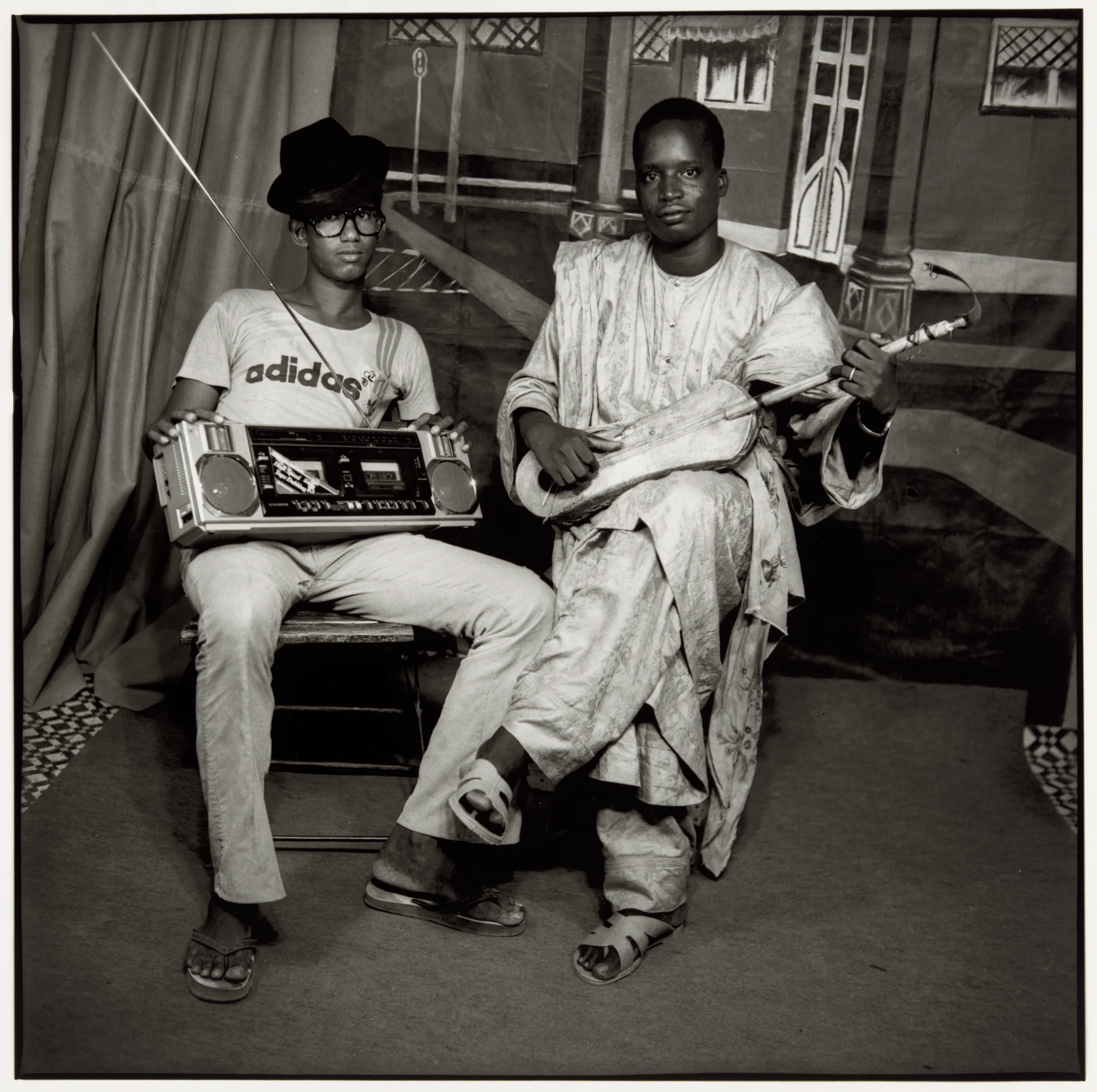 Black and white portrait of two men; one holds a boombox, the other a stringed instrument.