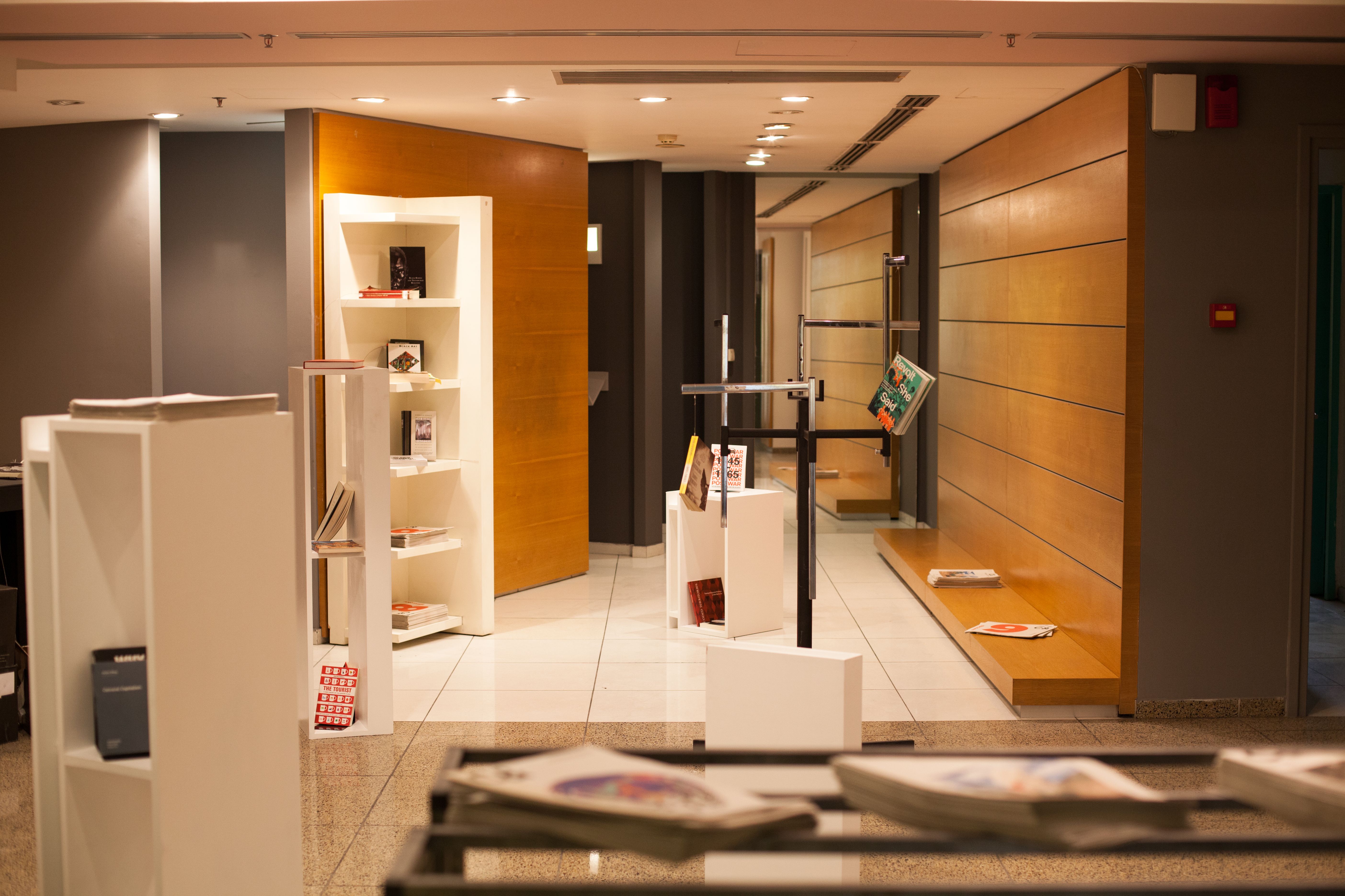 A modern interior space with books and magazines on white shelves and wood-paneled walls.