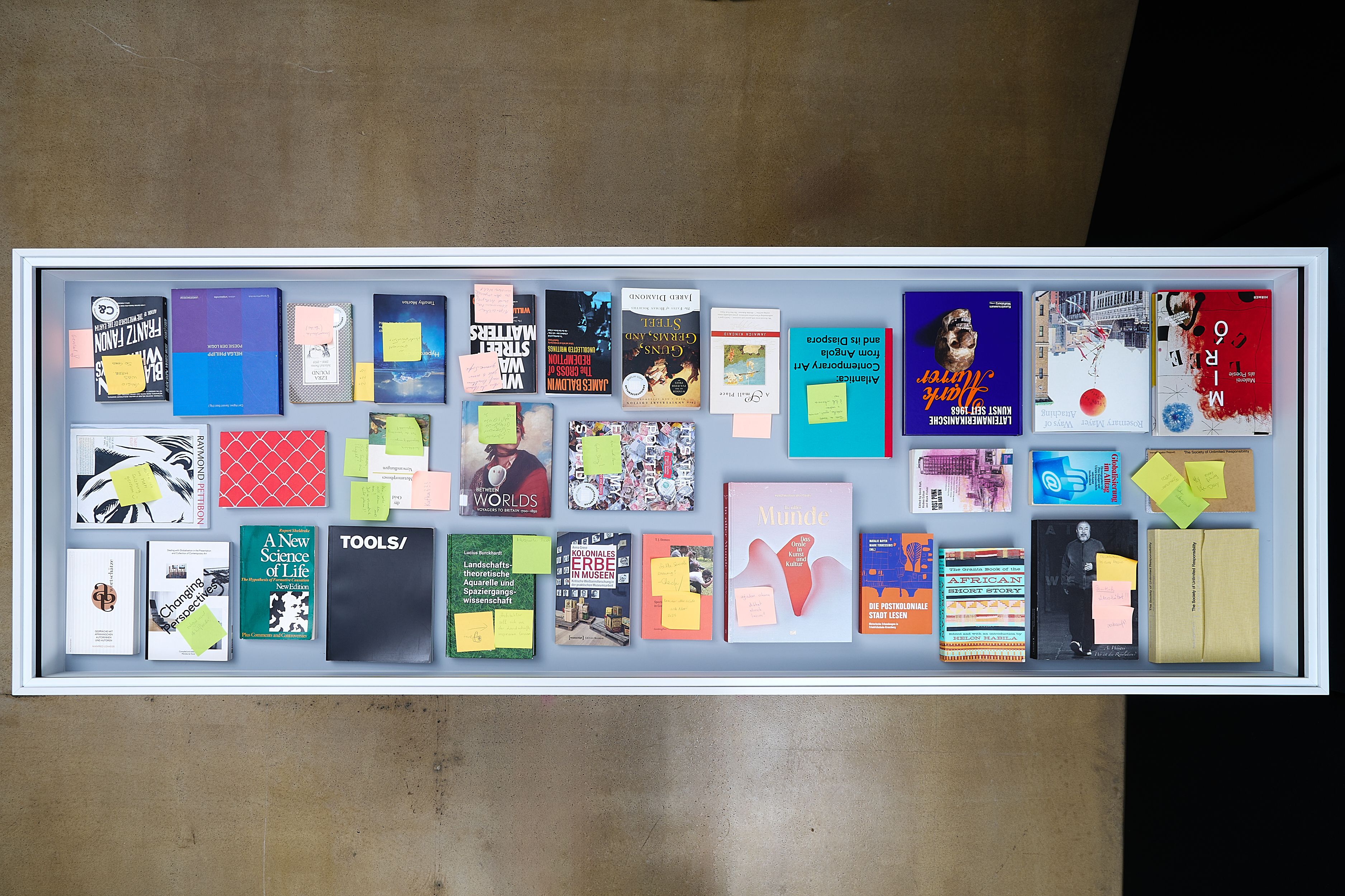 Overhead view of a white display case filled with books and magazines, many marked with sticky notes.