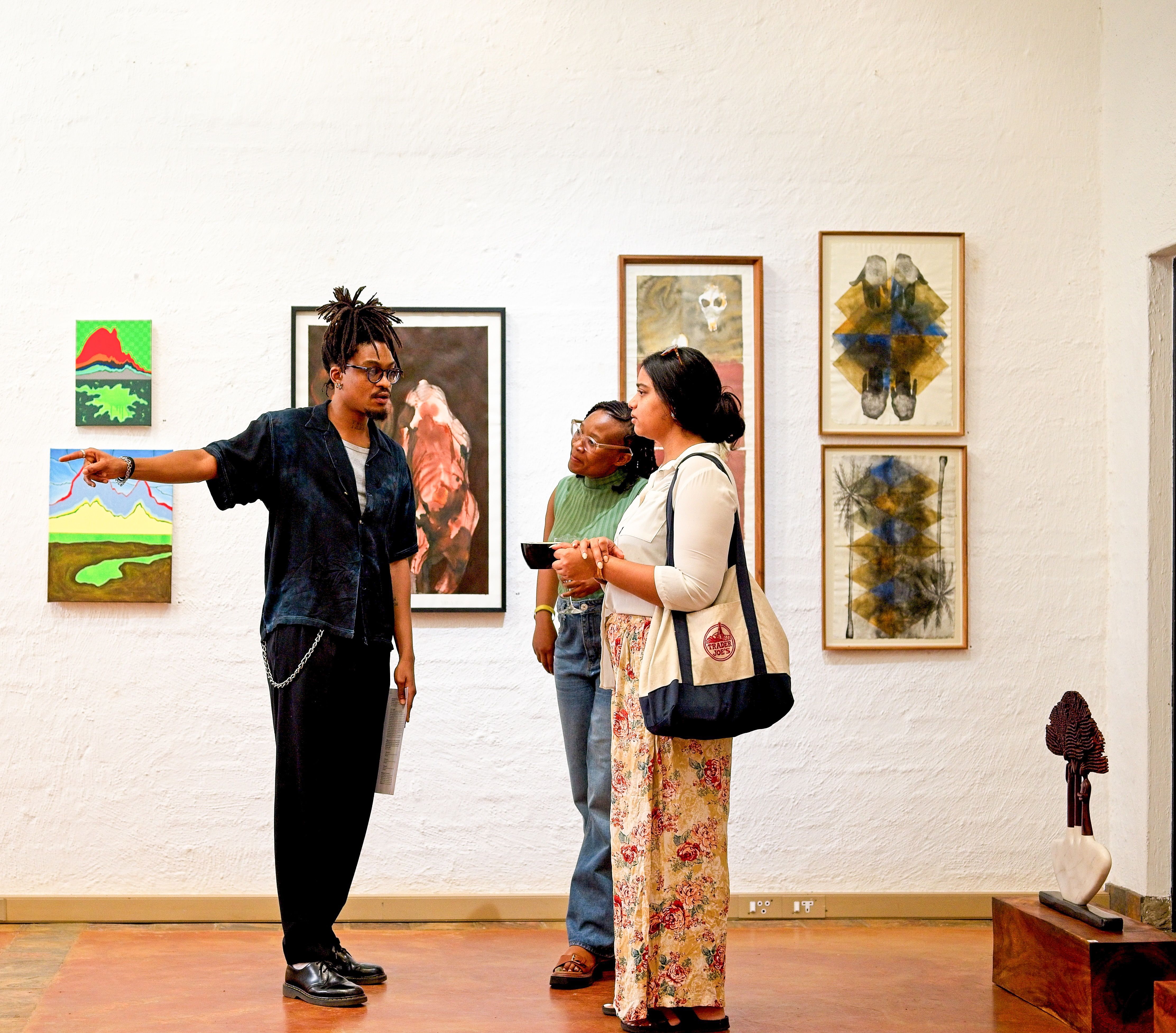A man points to artwork on a white wall for two women in a gallery.