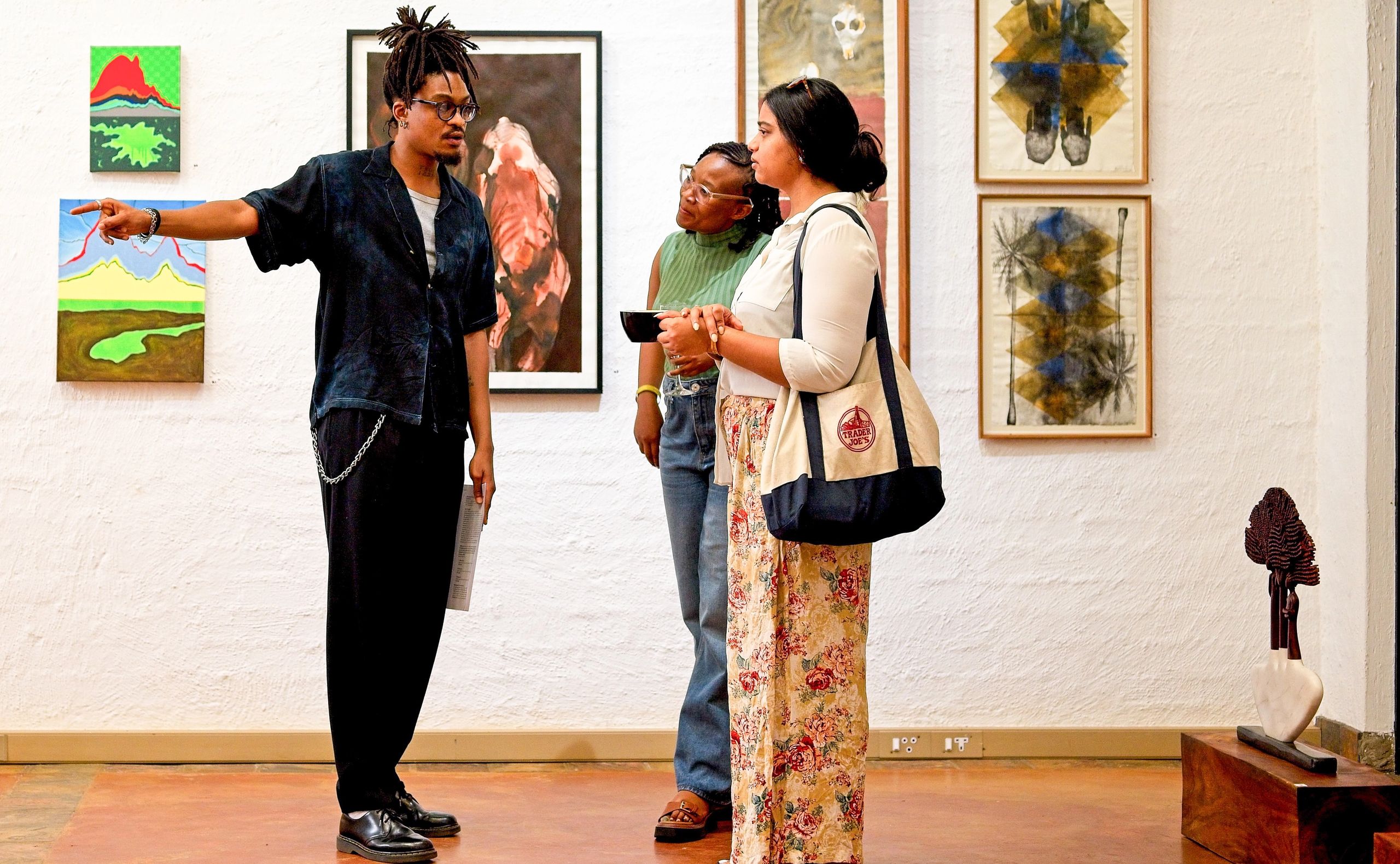 A man points to artwork on a white wall for two women in a gallery.