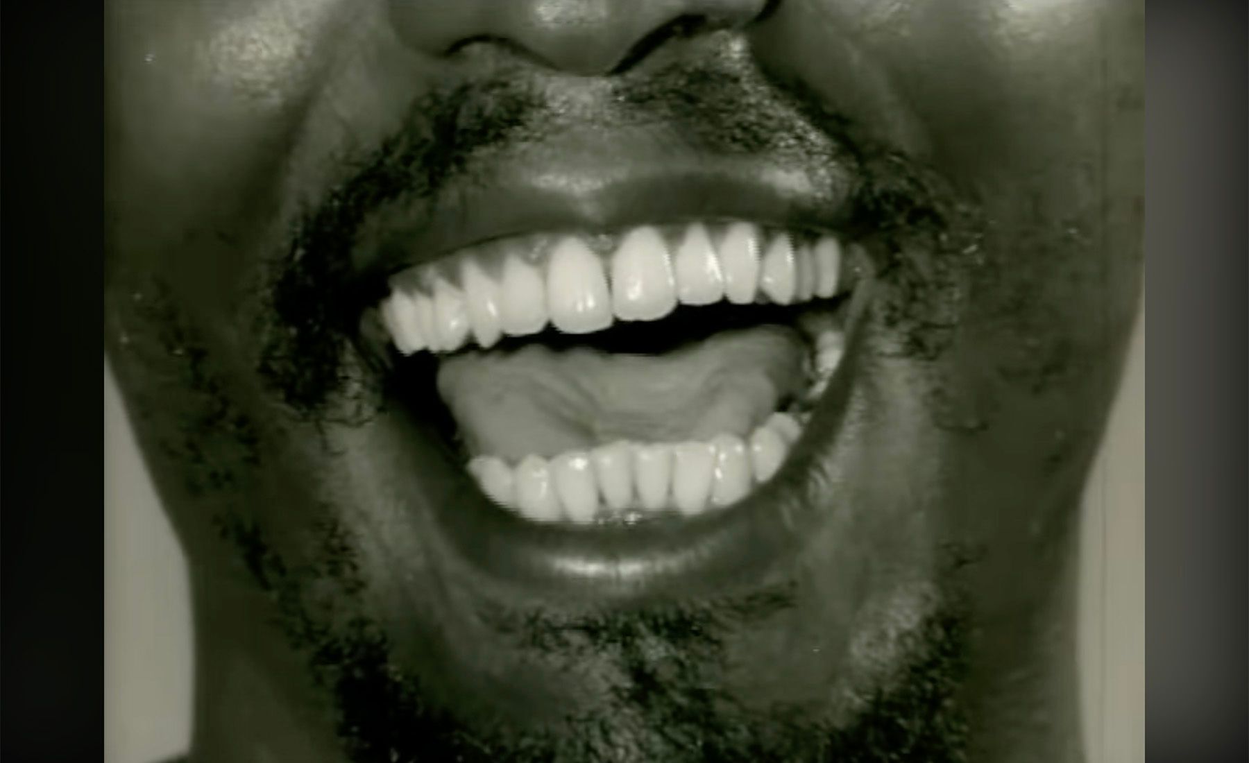 Monochrome close-up of a bearded man laughing, showing white teeth.