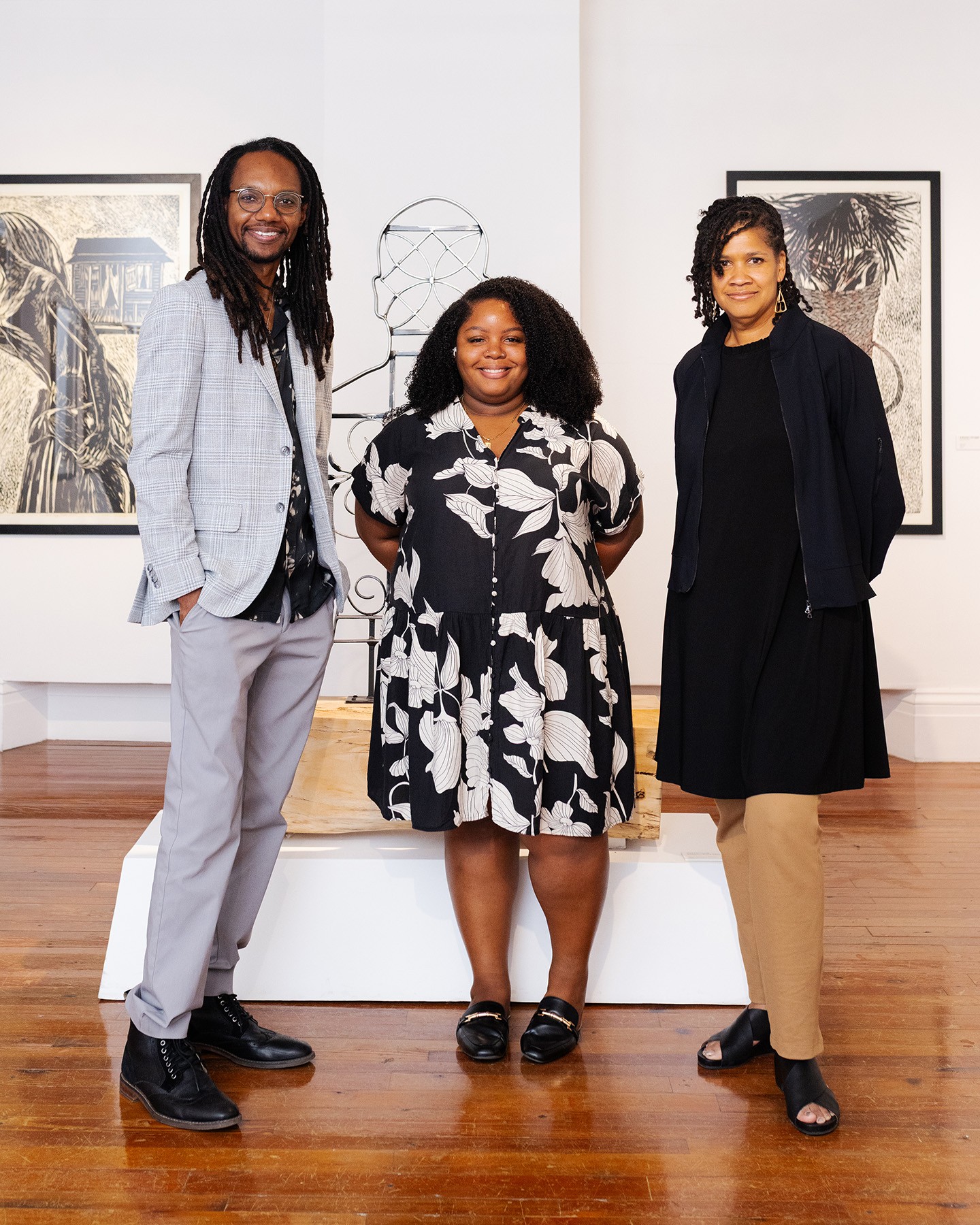 Three Black individuals, two women and one man, smile in an art gallery.
