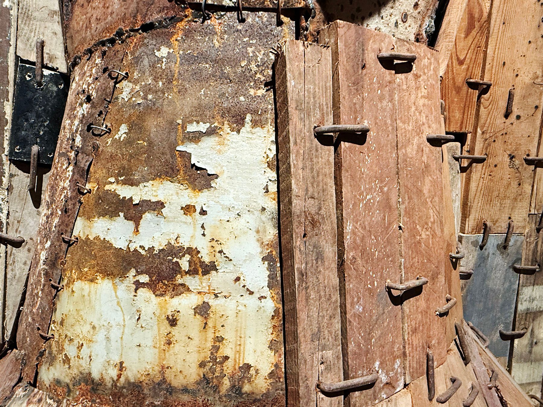 Weathered surface of rusted metal with peeling paint and wooden planks covered in bent nails.