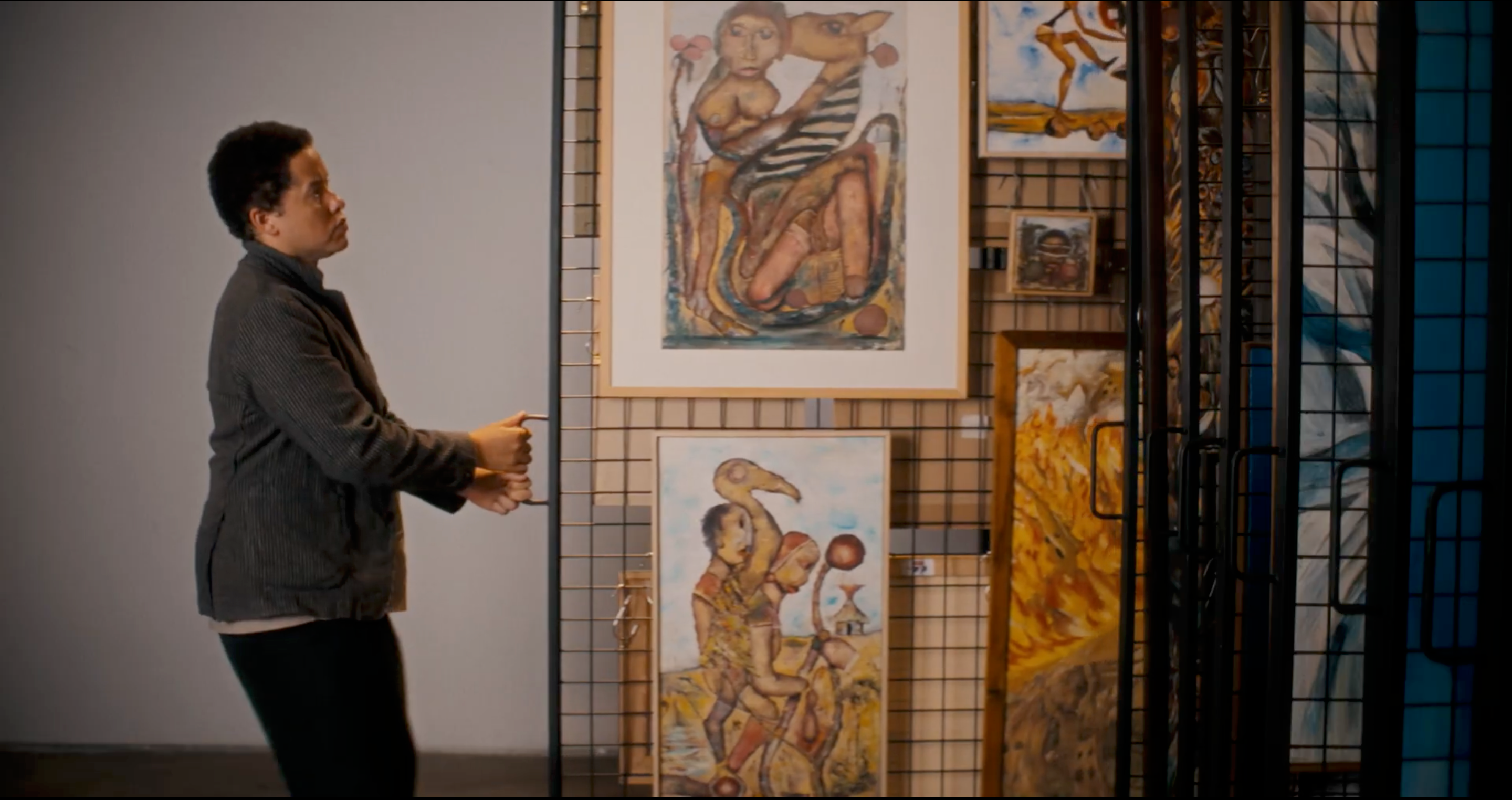 A woman with short dark hair looks at paintings displayed on a grid wall, her hands near the display.