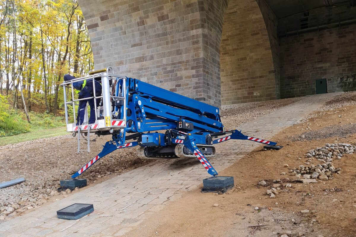 Plataforma aranha de lagartas com os quatro estabilizadores abertos, a trabalhar debaixo de um viaduto