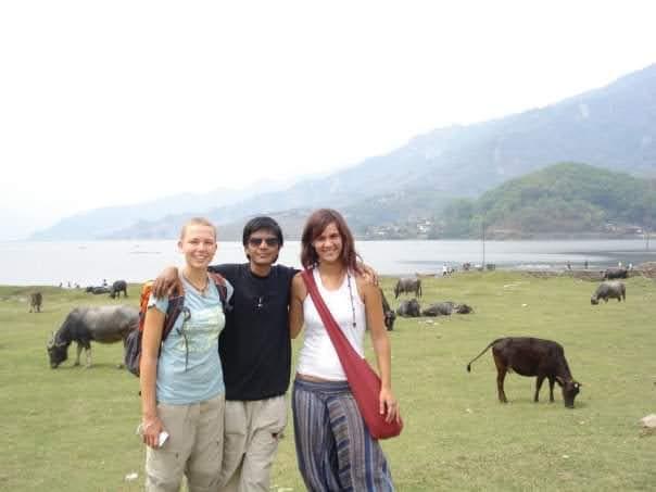 Saroj Khadgi standing with two travellers on a lakeside meadow
