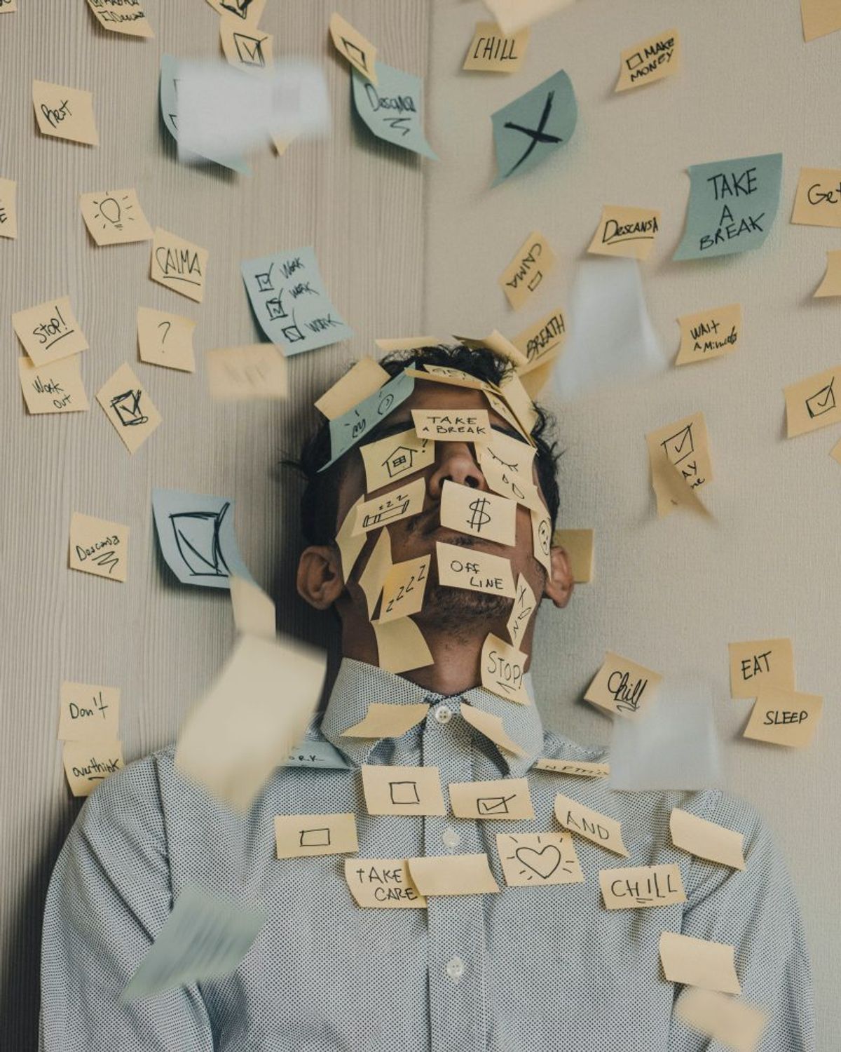 A man leaning against a wall with sticky notes over his face and up the wall