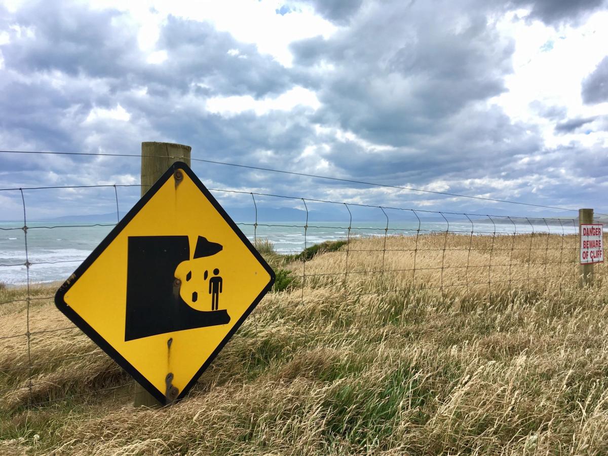 A yellow and black sign, warning of erosion, attached to a fence at the beach