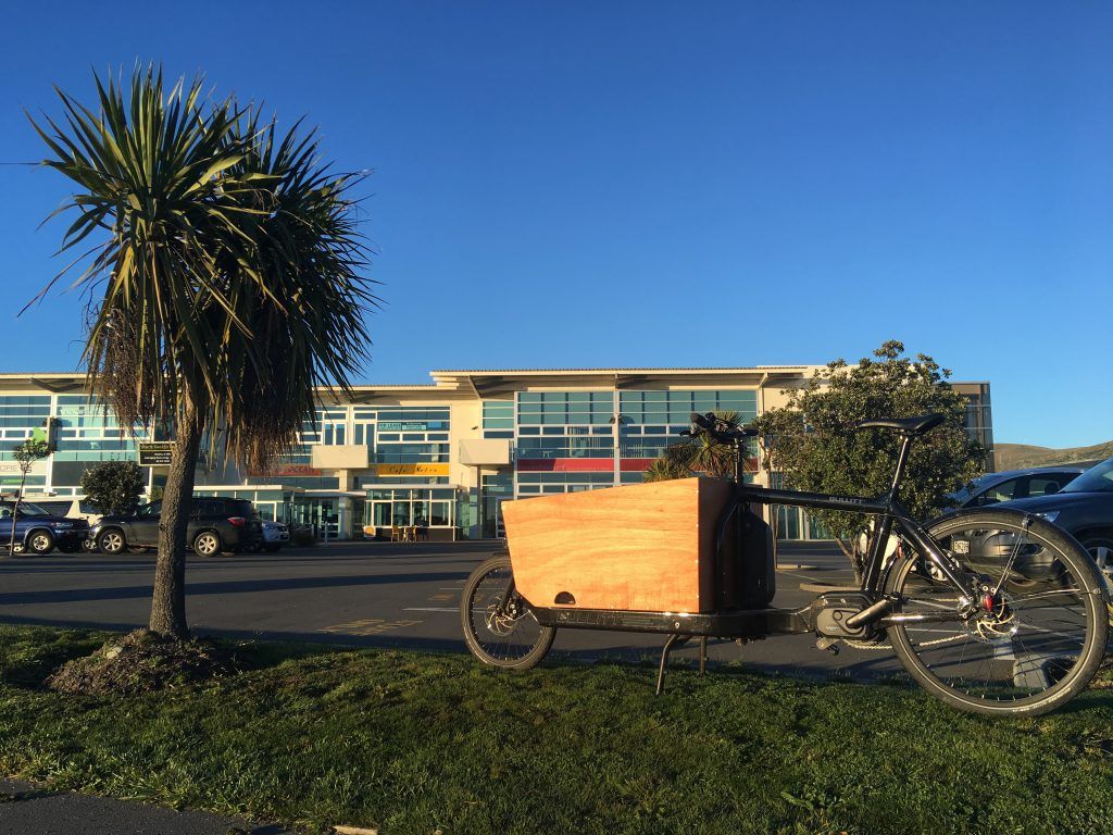 Bucket bike parked on grass curb with car park and office building in background