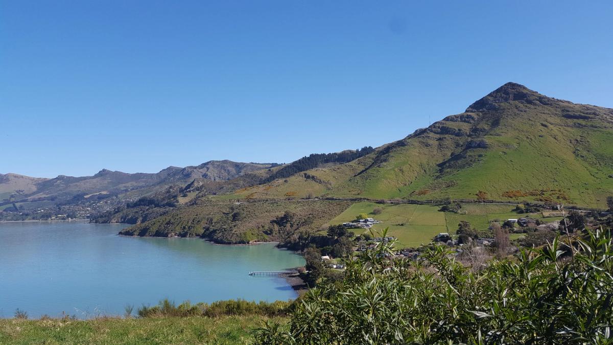 View of a bay with a small pier to the right, green farmland and a conical hill to the right
