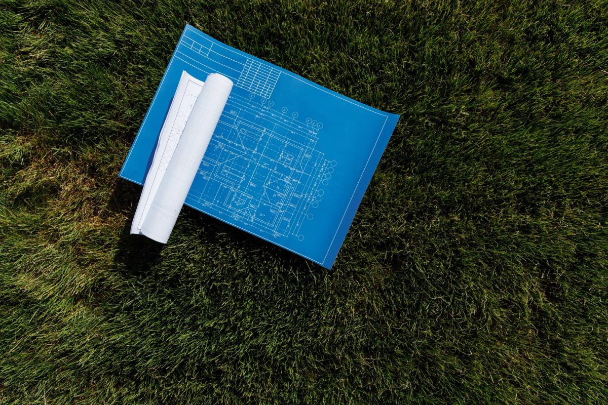 Unfurled blueprint on grass, rolled up plans lying on the left hand side of the blueprint