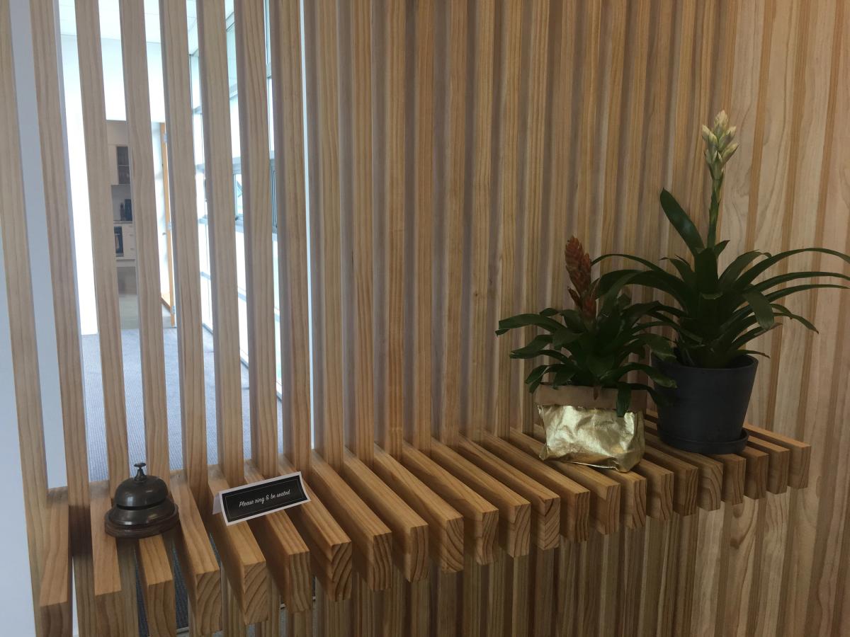 Timber screening and shelf holding a reception bell and two pot plants.