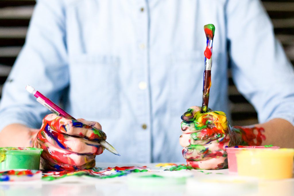 Person with painty hands, brush and pen at a table