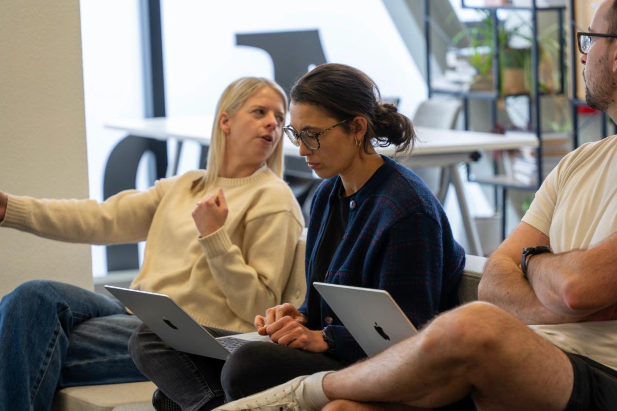 Group of people in conversation sitting on couches while holding laptops