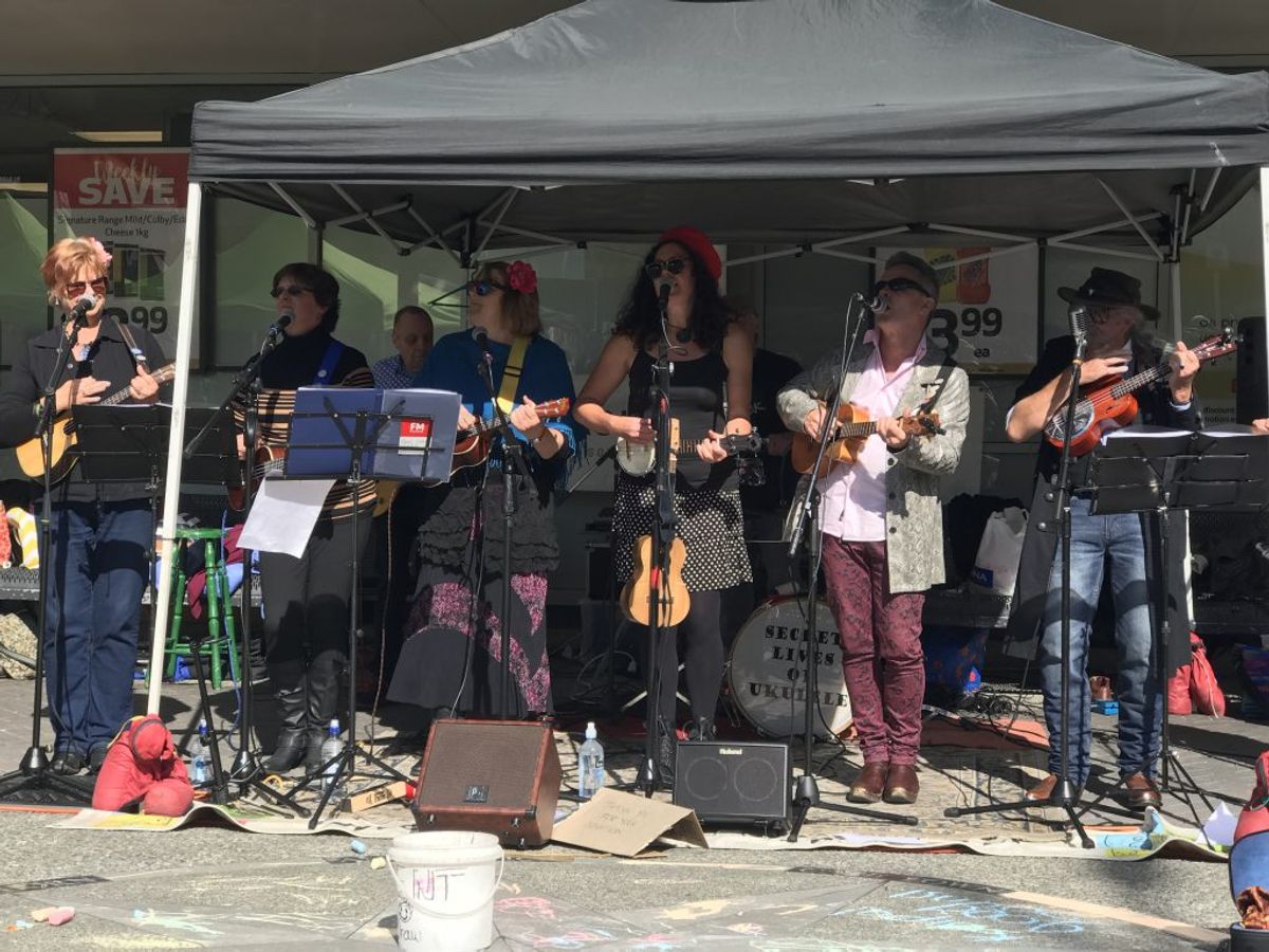 7 band members playing ukulele under a tent gazebo