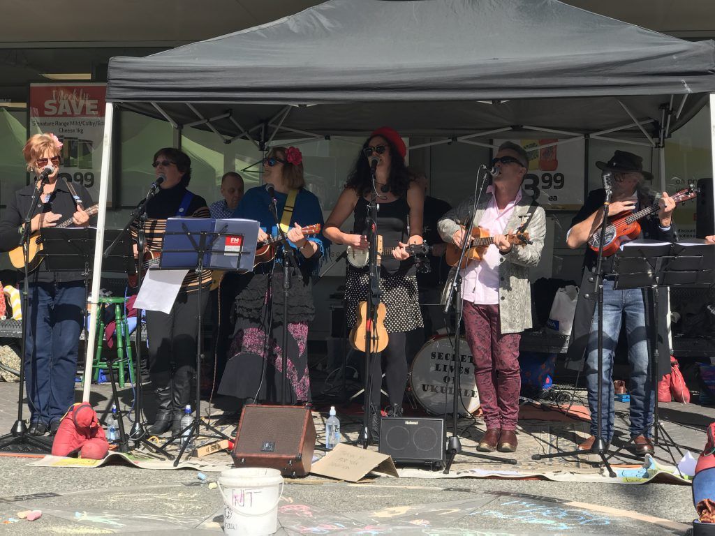 7 band members playing ukulele under a tent gazebo