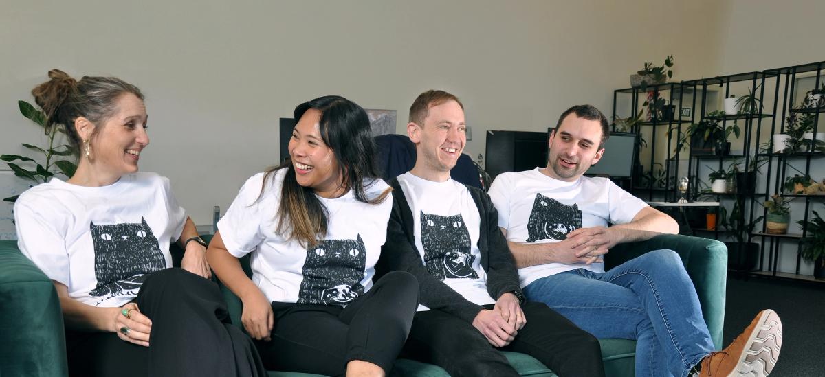 Four people sitting laughing on a couch wearing MadeCurious tee shirts