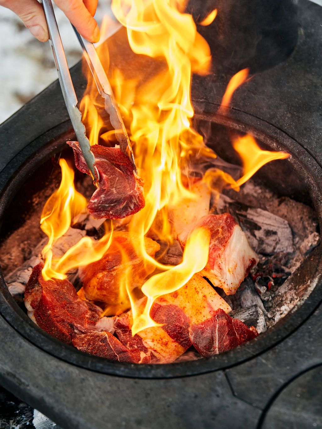 Kjøttet stekes rett på glørne. Det vil komme flammer og røyk, så sørg for å ha en lang klype – det blir varmt!
