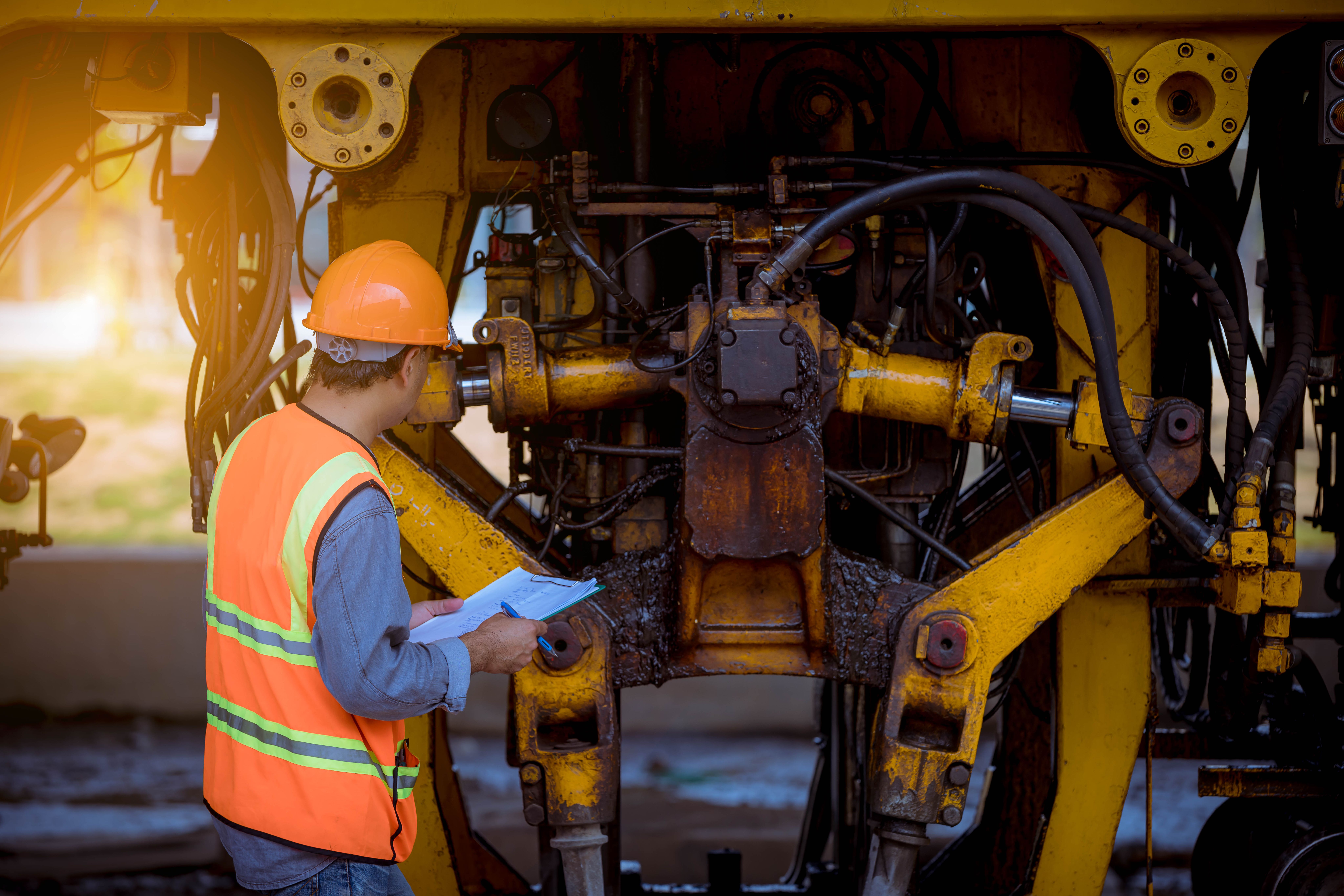 a construction worker is working on a machine and looking at a clipboard .