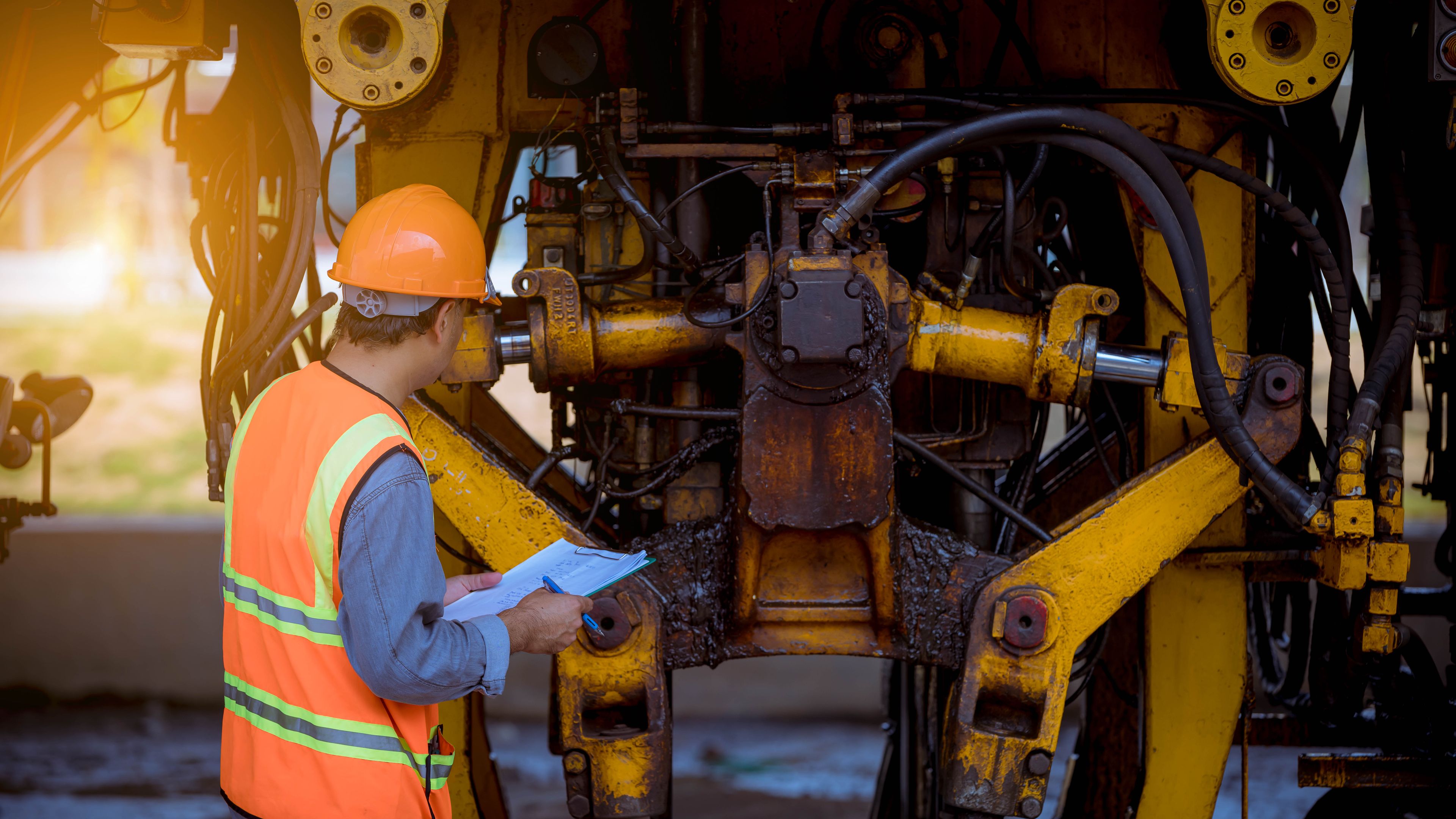 a construction worker is working on a machine and looking at a clipboard .