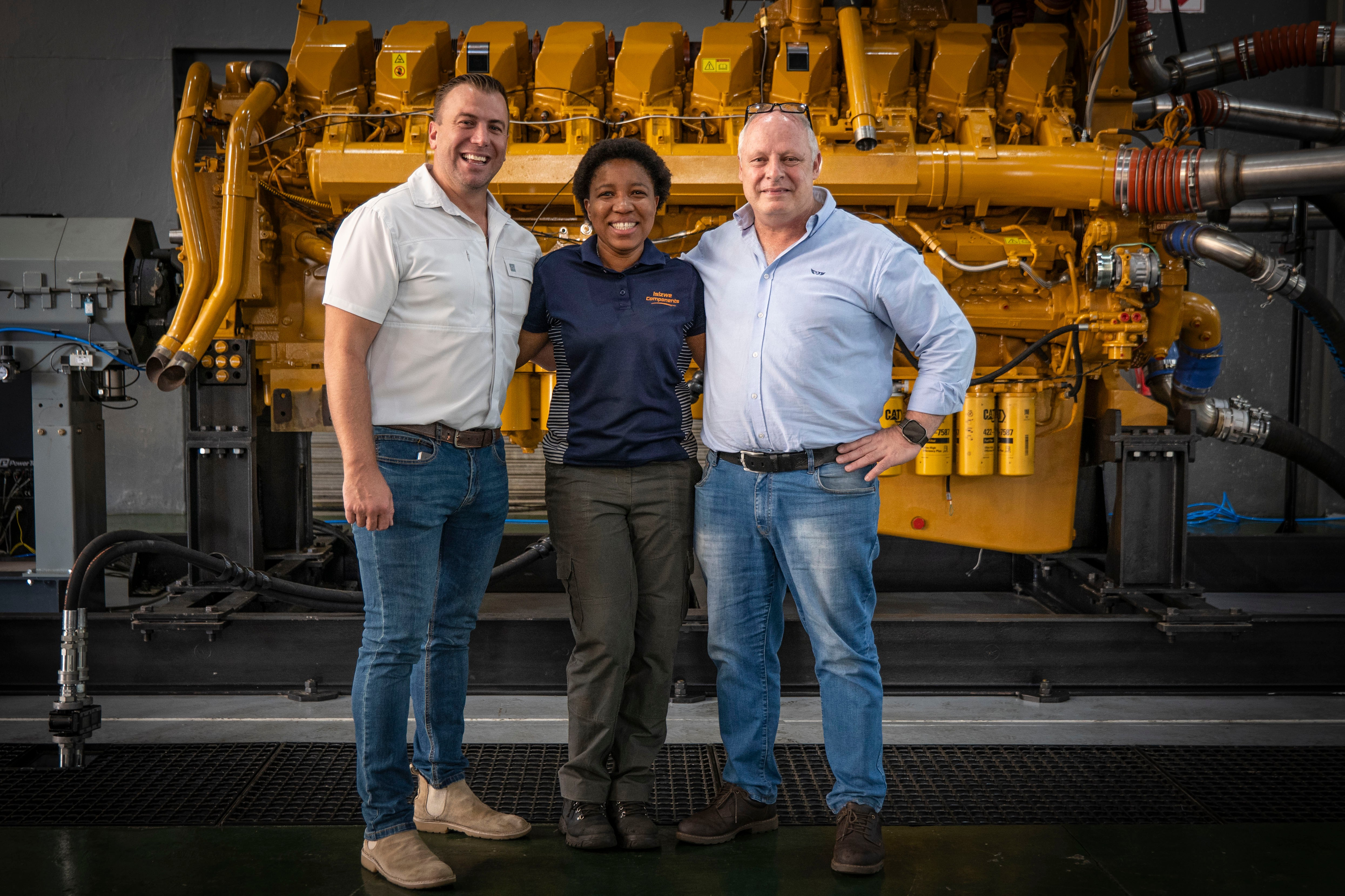 three men and a woman are posing for a picture in front of a large engine .