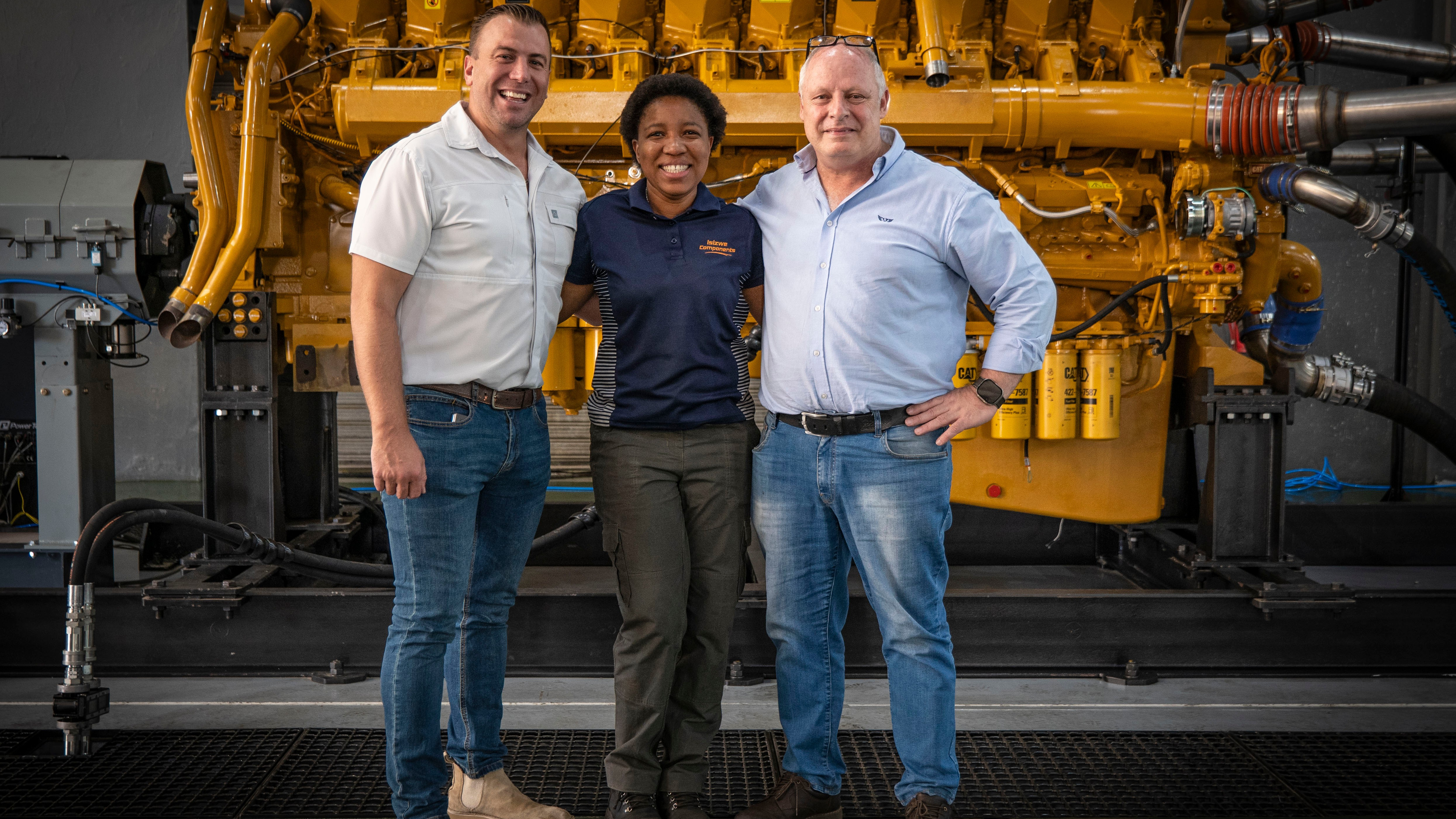 three men and a woman are posing for a picture in front of a large engine .