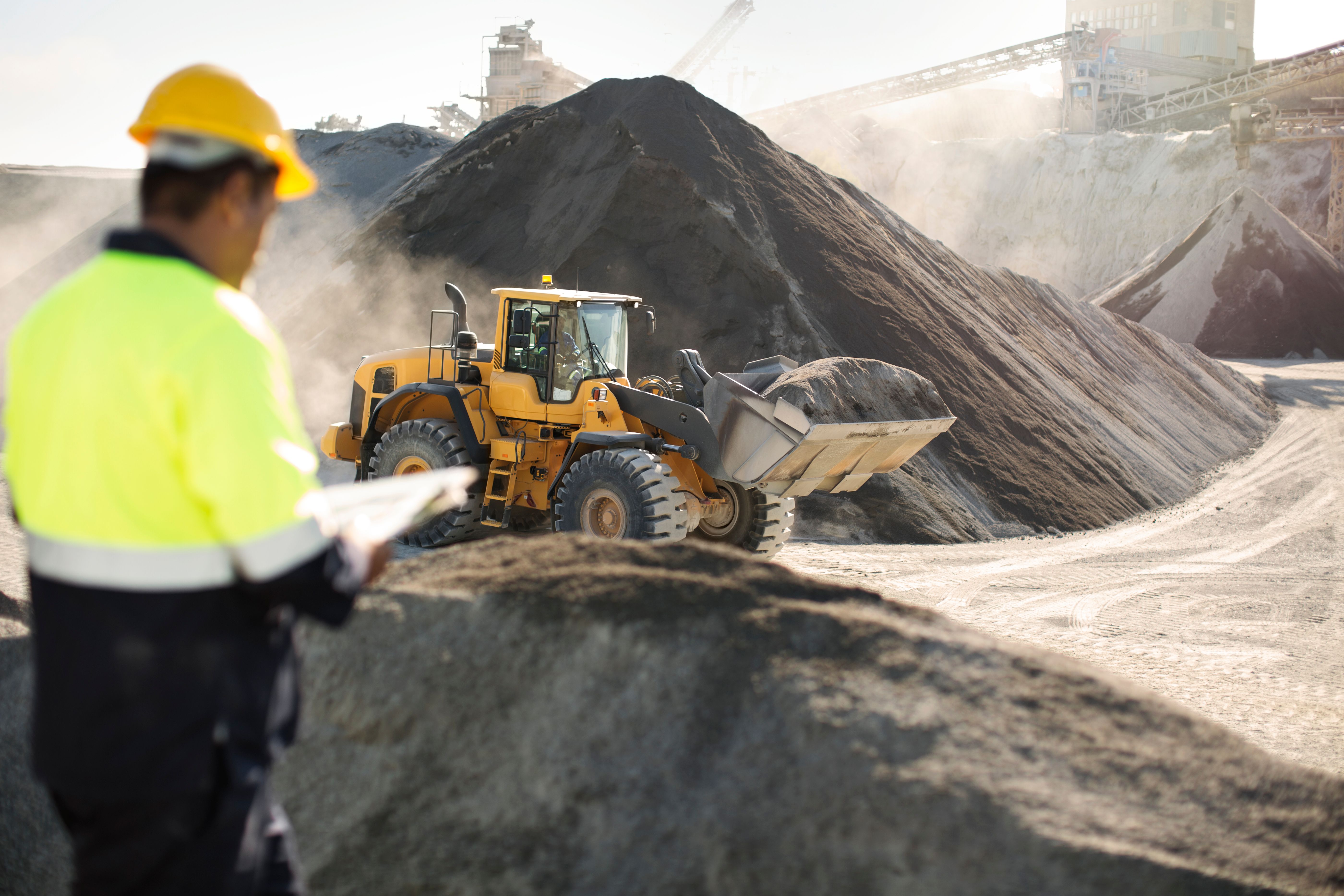a man is standing in front of a pile of dirt and a bulldozer .