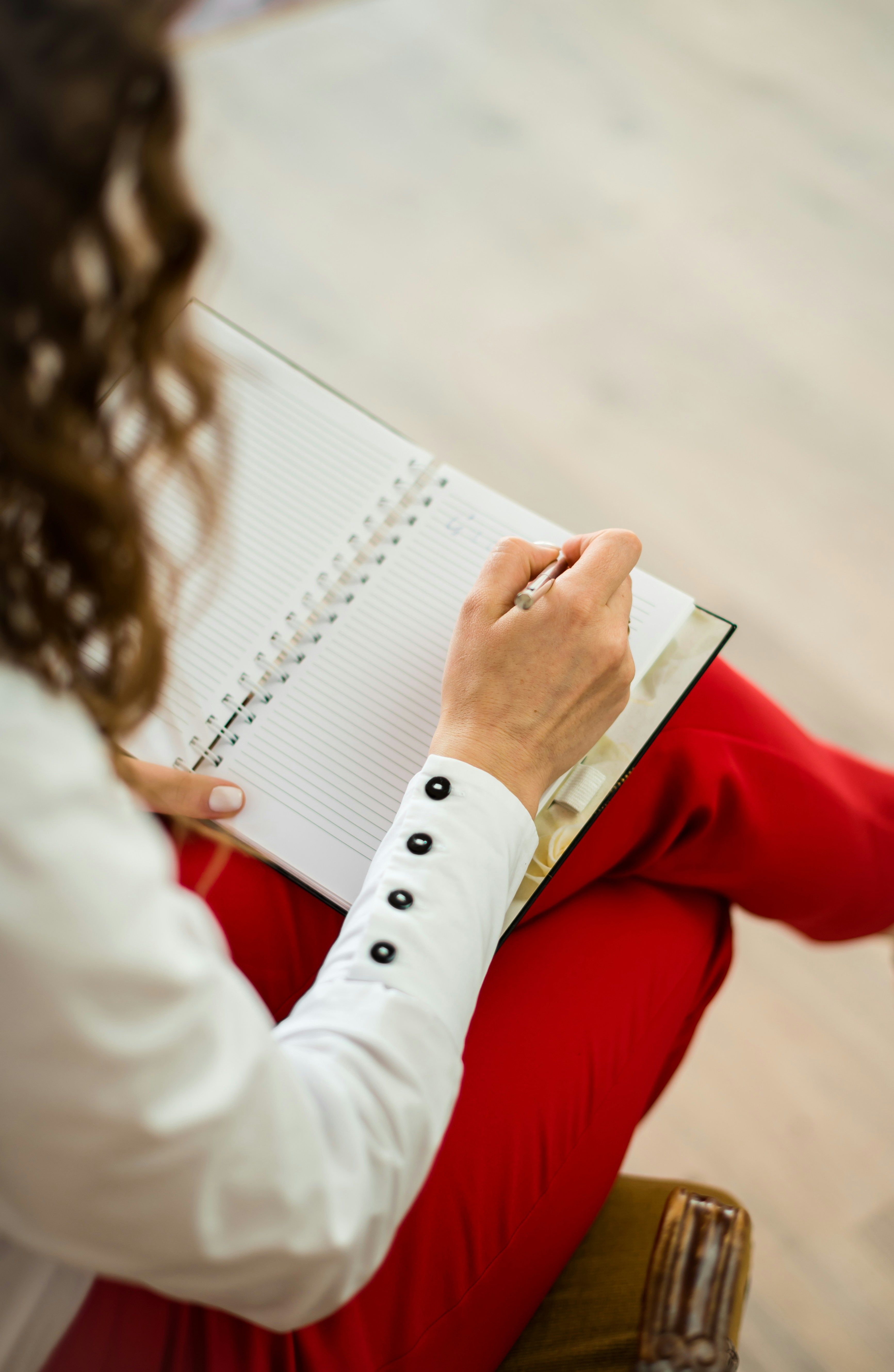 A person writes in an open notebook on their lap, viewed from behind.