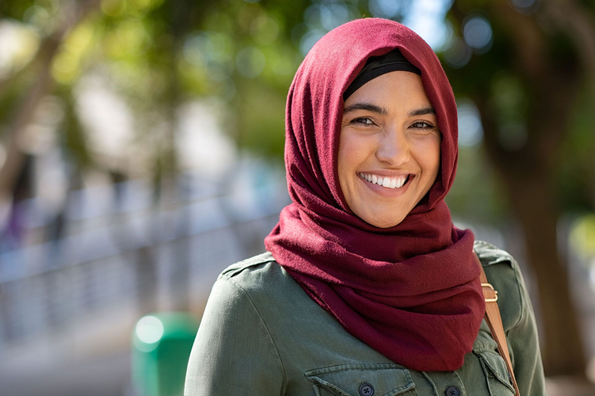 Portrett av en smilende kvinne med mørkerød hijab utendørs.