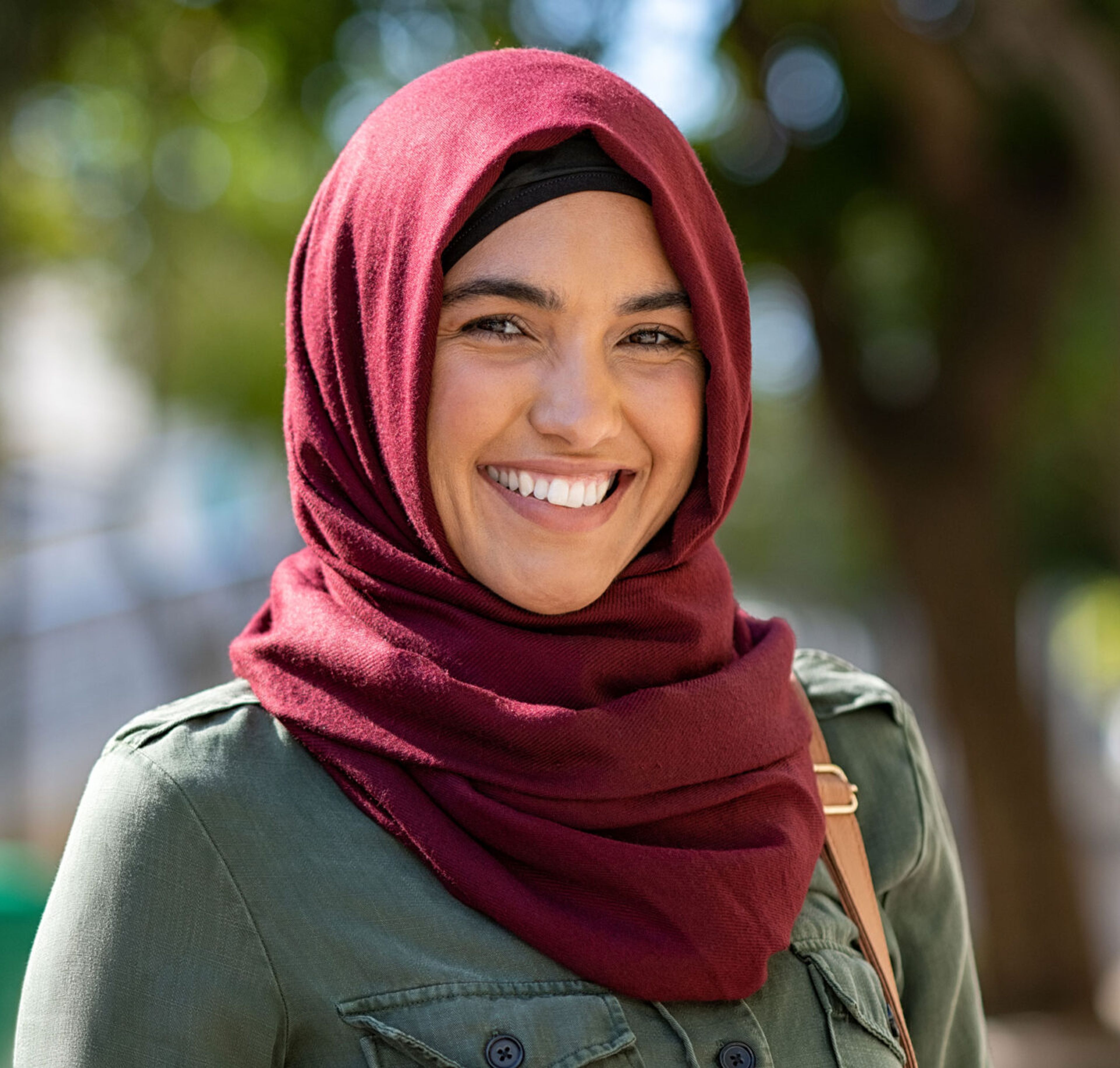 Portrett av en smilende kvinne med mørkerød hijab utendørs.