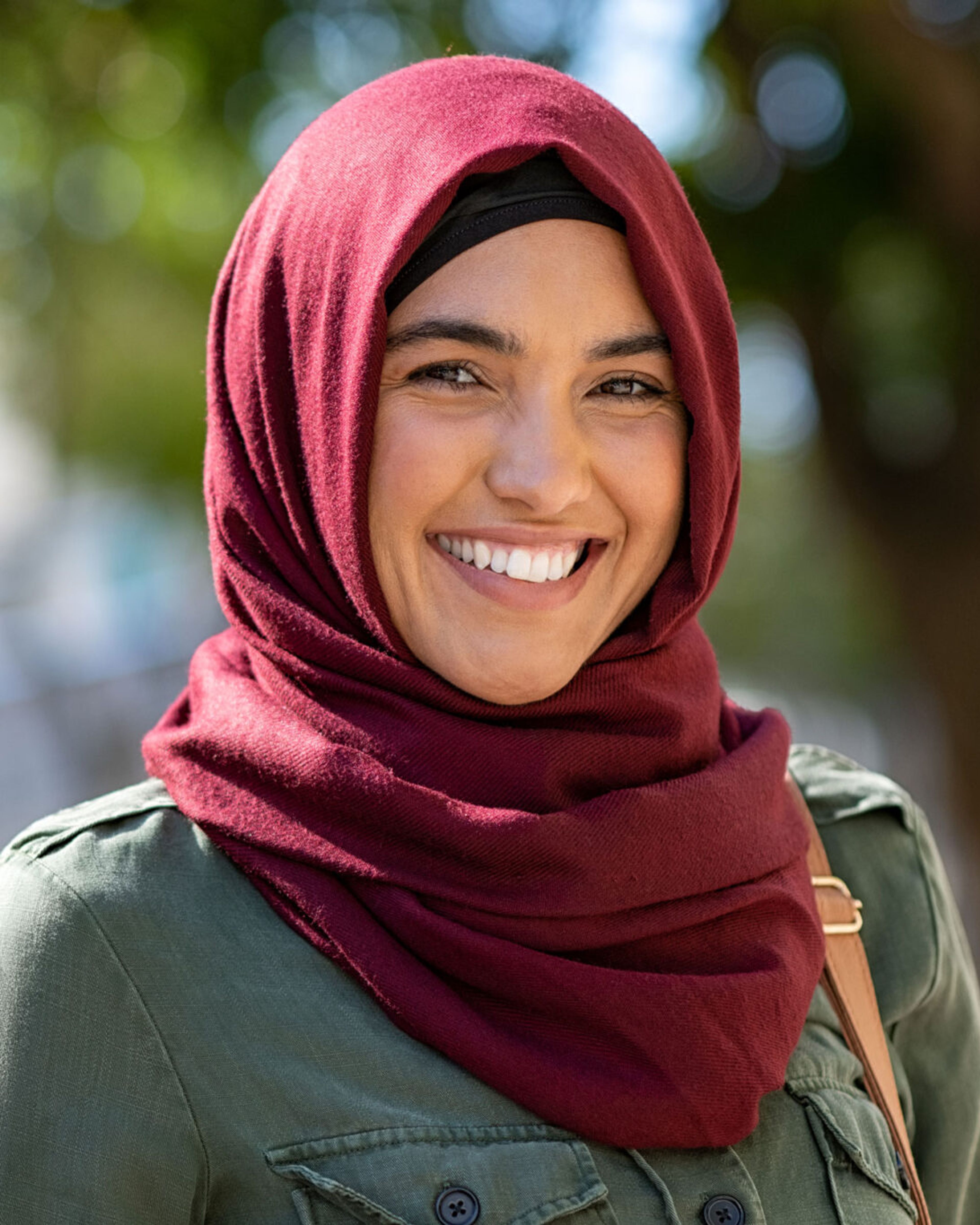 Portrett av en smilende kvinne med mørkerød hijab utendørs.