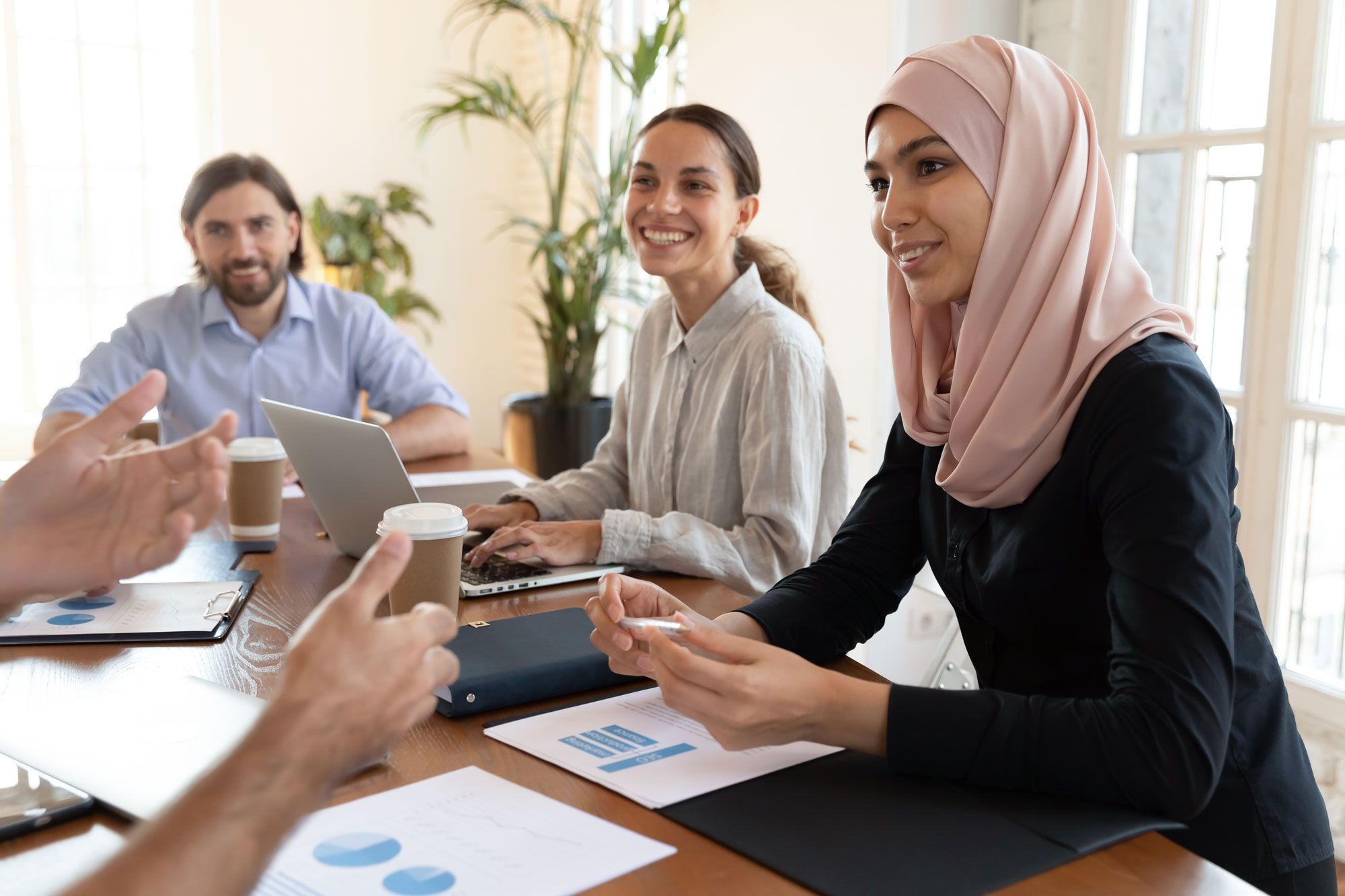 Flere personer i et møte rundt et bord, blant dem en kvinne med rosa hijab.